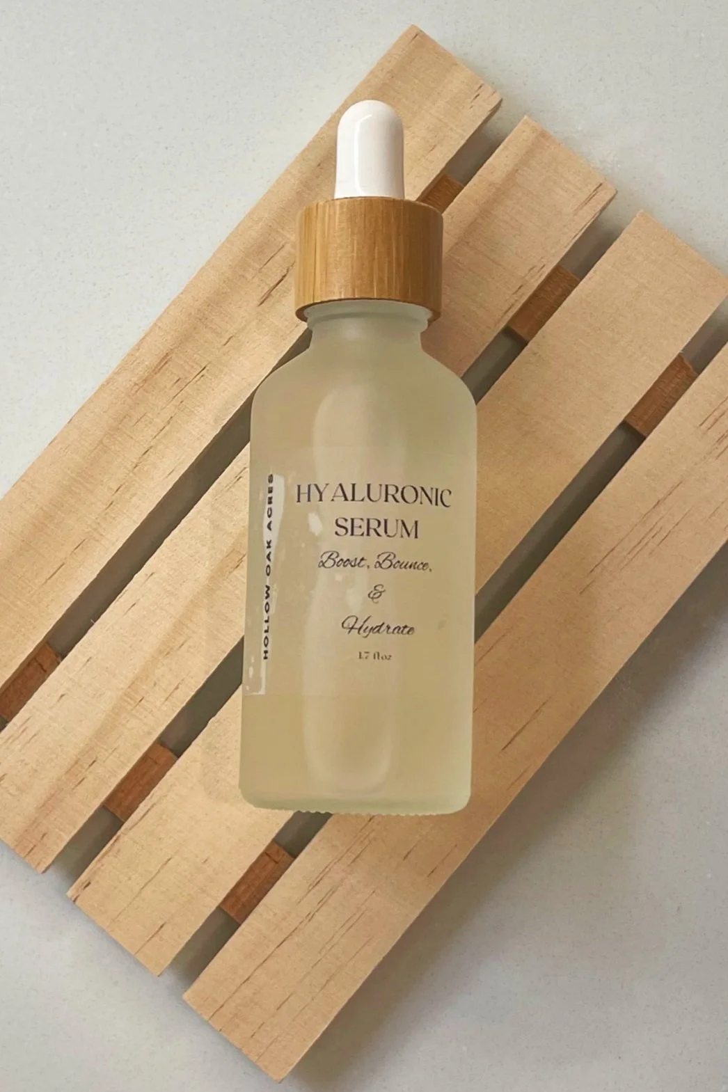 A frosted glass bottle of hyaluronic serum with a wooden dropper cap, placed on a light wood slatted surface.