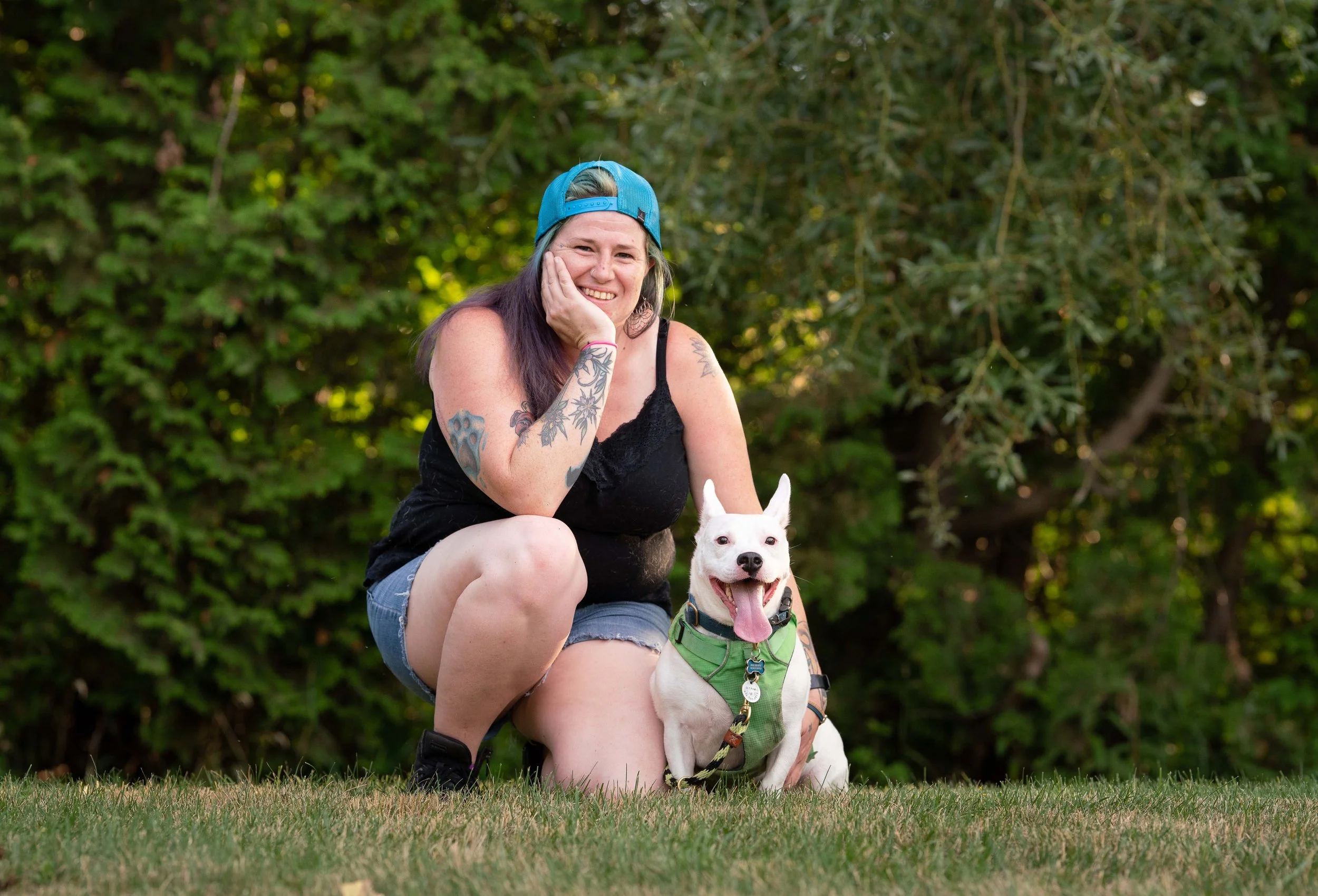 Laurie weating a blue baseball hat is kneeling with a medium white dog with pricked ears on her left hand