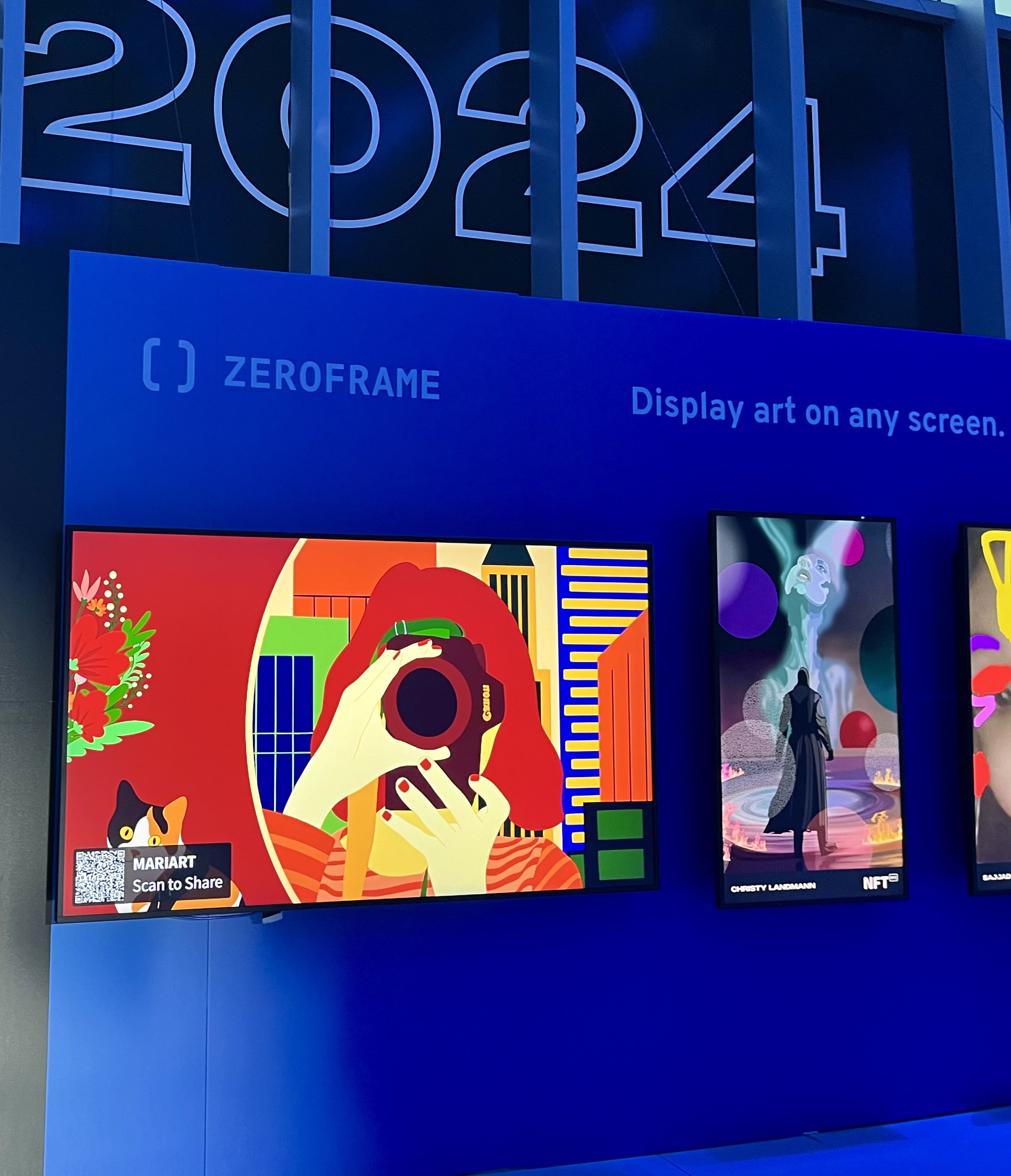 Digital art display showcasing colorful illustrations, including a person with a camera, and abstract designs, under a 'ZeroFrame' banner. '2024' is visible above the displays.
