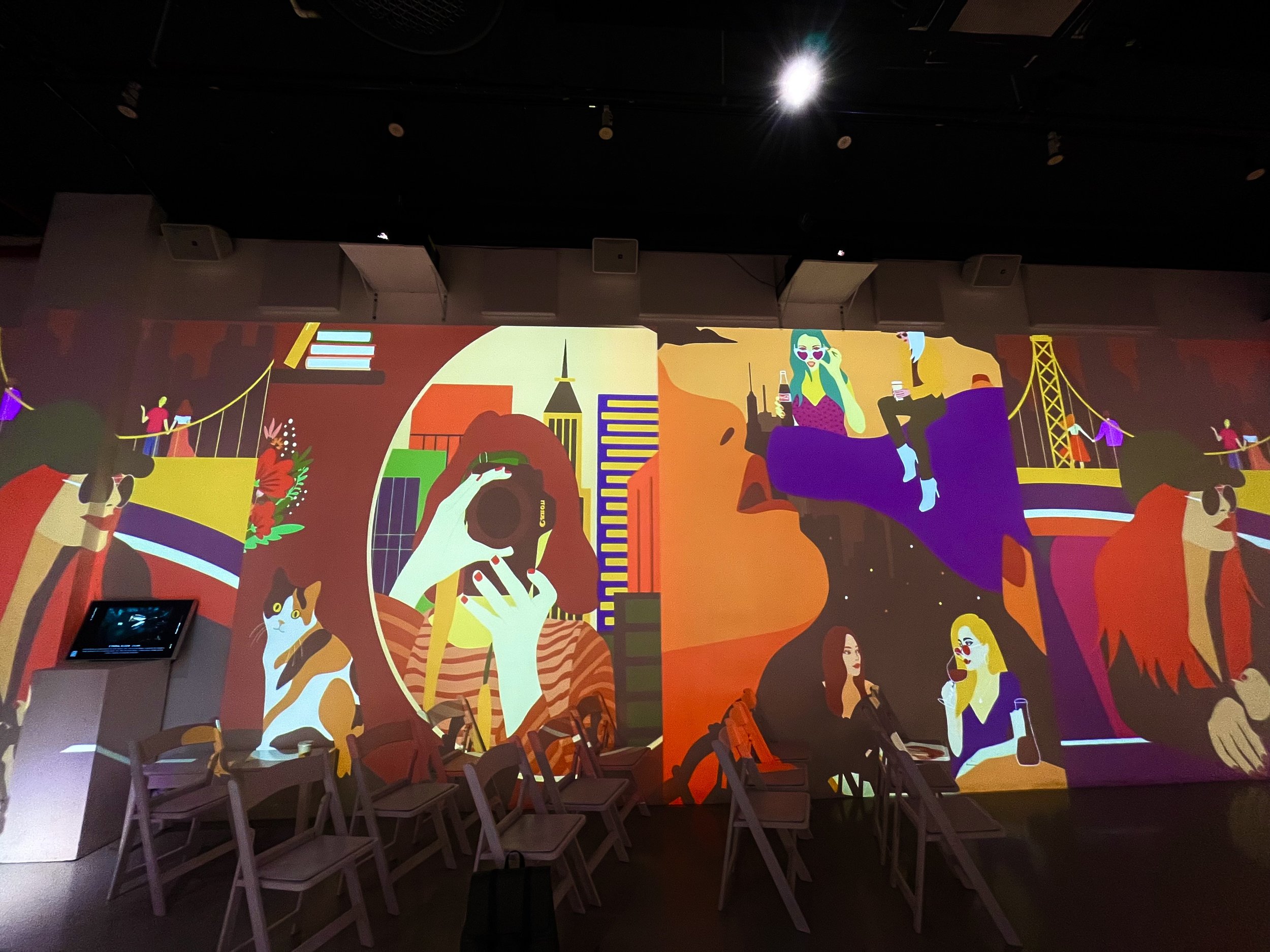 Colorful abstract wall mural with women, cameras, bridges, and a cat.