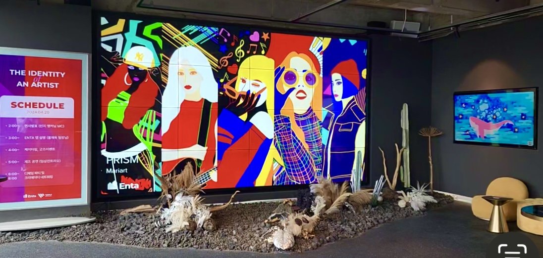 Colorful mural depicting abstract figures and musical symbols, with a schedule poster on the left and desert plants below.