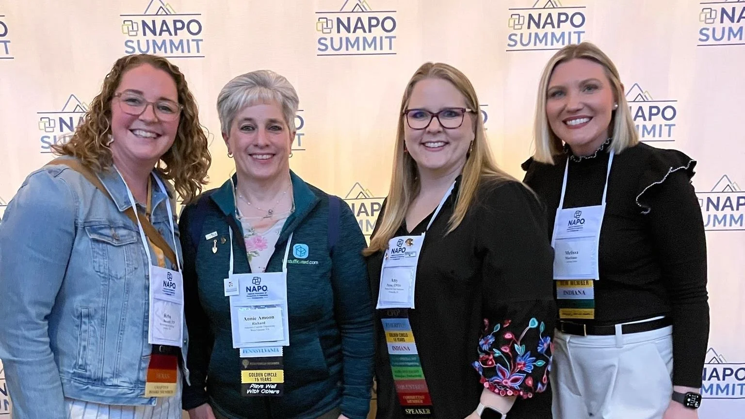 A group of four women standing in front of the NAPO Summit banner.