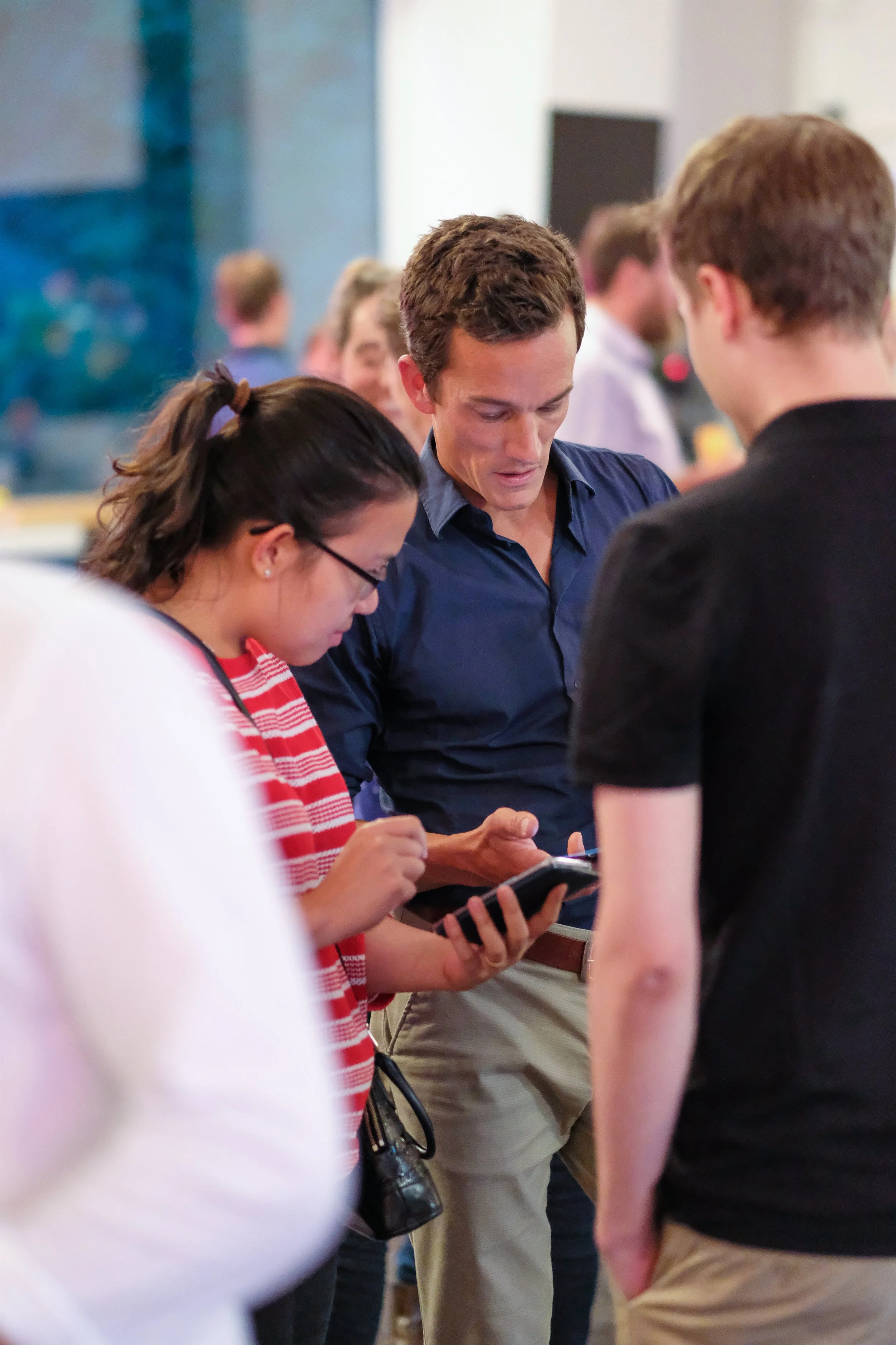 Drei Menschen, die in einer Menschenmenge stehen, wobei ein Mann ein Smartphone hält und die anderen beiden Personen den Bildschirm betrachten.