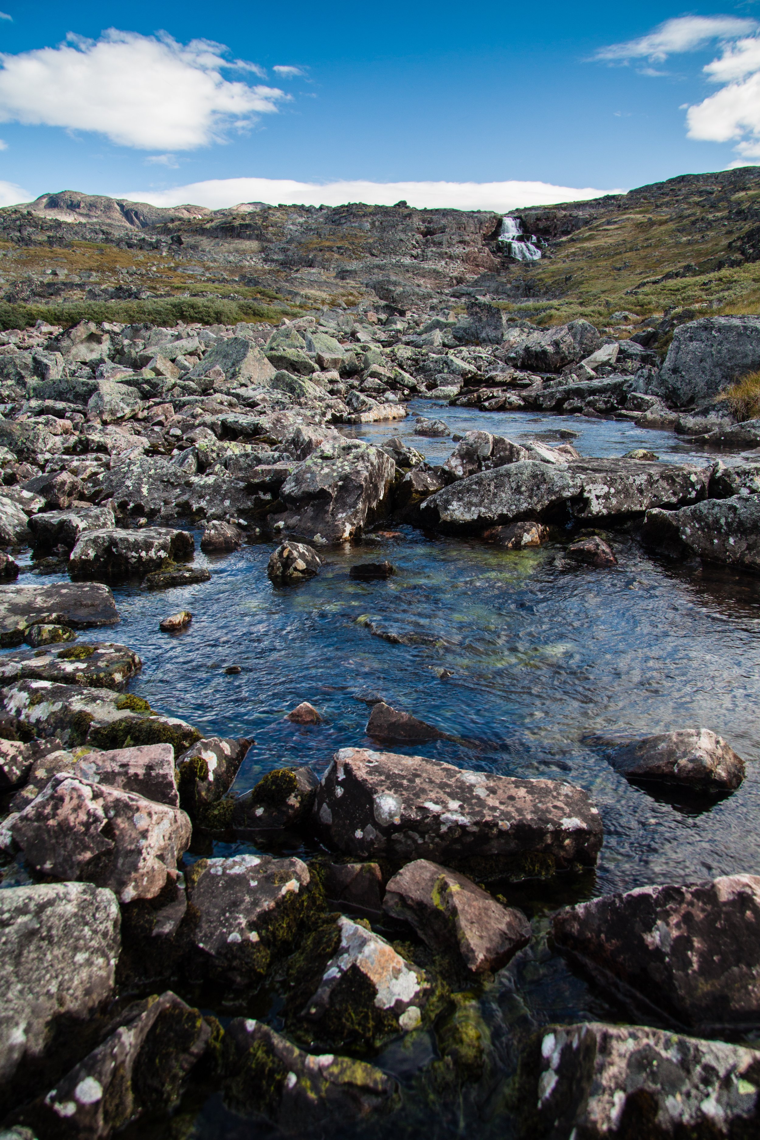 Ein Fluss fließt durch eine felsige Landschaft unter einem blauen Himmel mit wenigen Wolken.