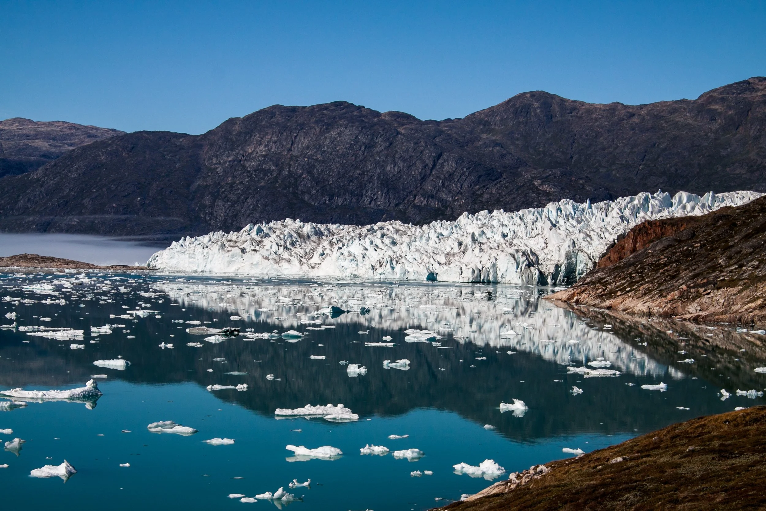 Gletscher mit Eisschollen im Wasser vor Bergen.