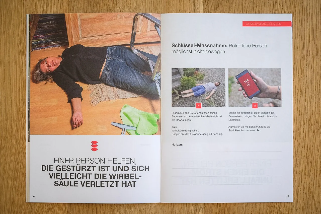 Offenbar eine Broschüre mit Erste-Hilfe-Maßnahmen gegen Wirbelsäulenschmerzen, mit einem Bild einer bewusstlosen Person, die auf dem Boden liegt, und Anweisungen zur Lagerung und Benachrichtigung der Notrufnummer 144.