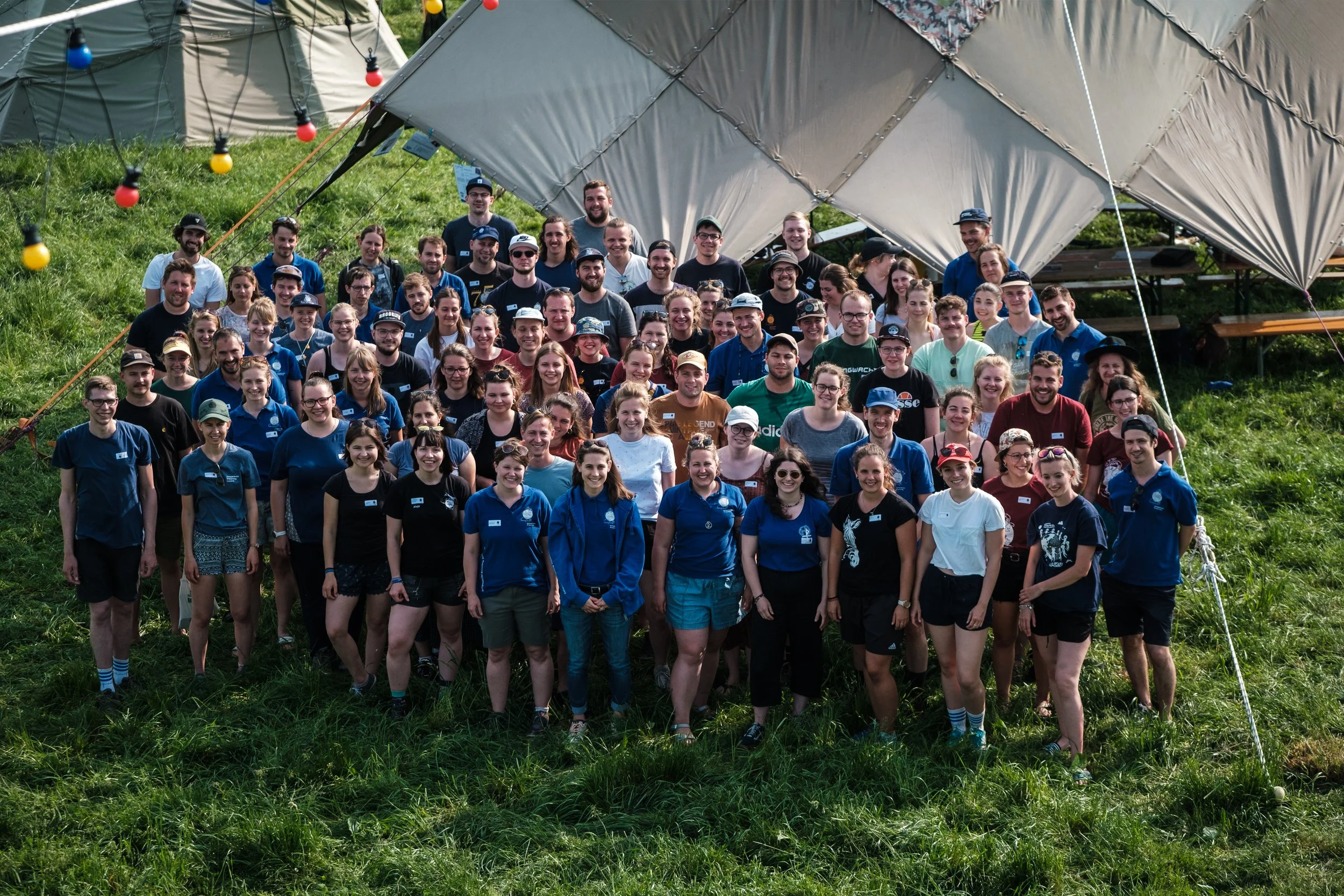 Gruppe von Menschen im Freien vor einer großen Zeltstruktur, alle lächeln und posieren für das Foto.