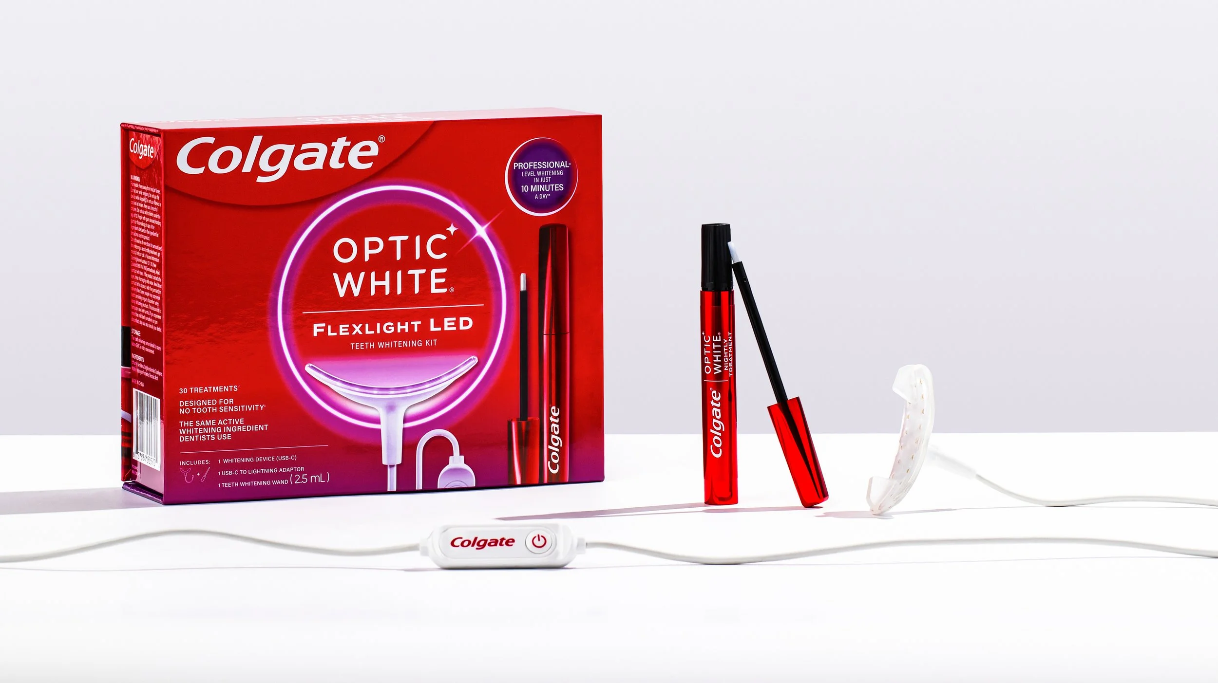 Colgate Optic White Flexlight LED teeth whitening kit with LED device, whitening gel pen, whitening wand, and mouthpiece, displayed on a white surface against a gray background.