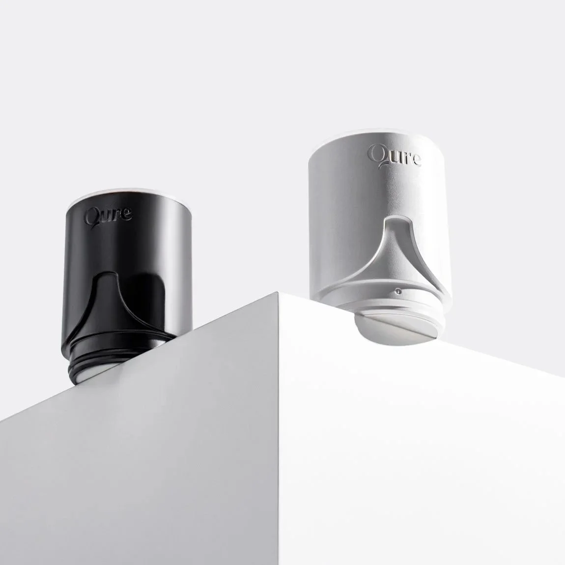 Two Puré speaker devices, one black and one white, placed on a white corner of a wall with a minimalist background.