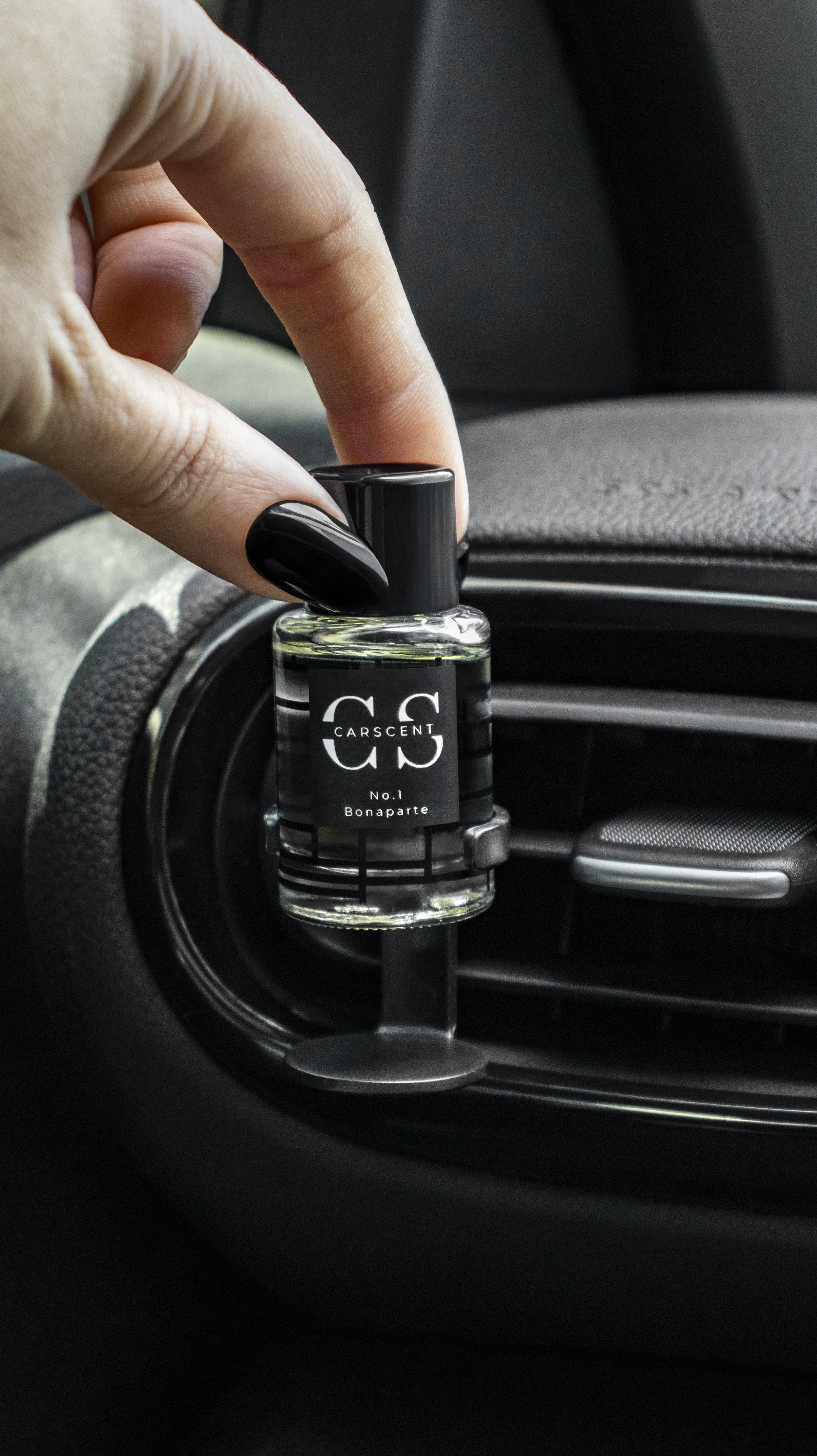 Hand placing a Carscent No. 1 Bonaparte car air freshener next to a vehicle air vent.