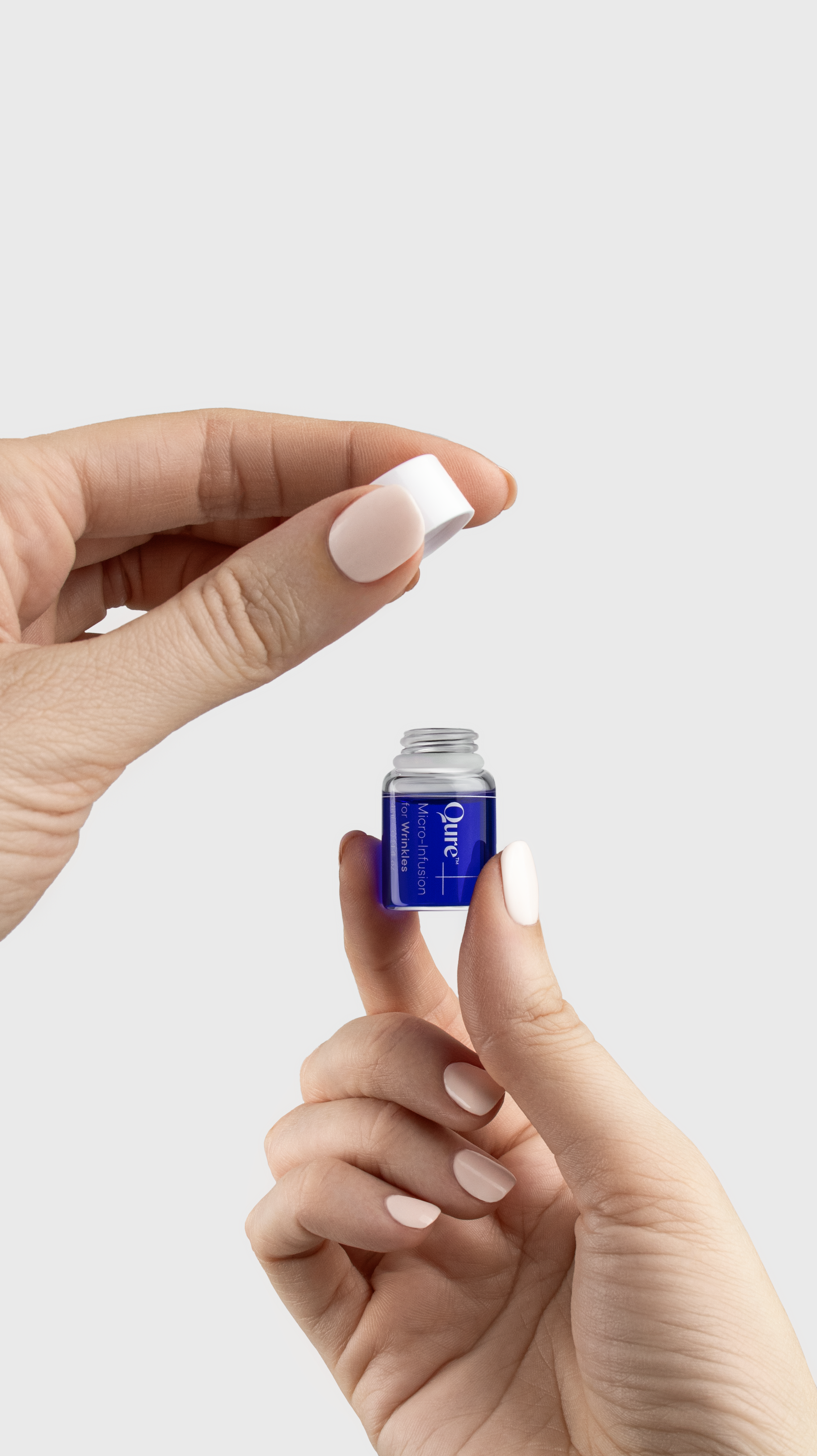Person holding a small blue and silver bottle of Qure Micro-Infusion skincare product