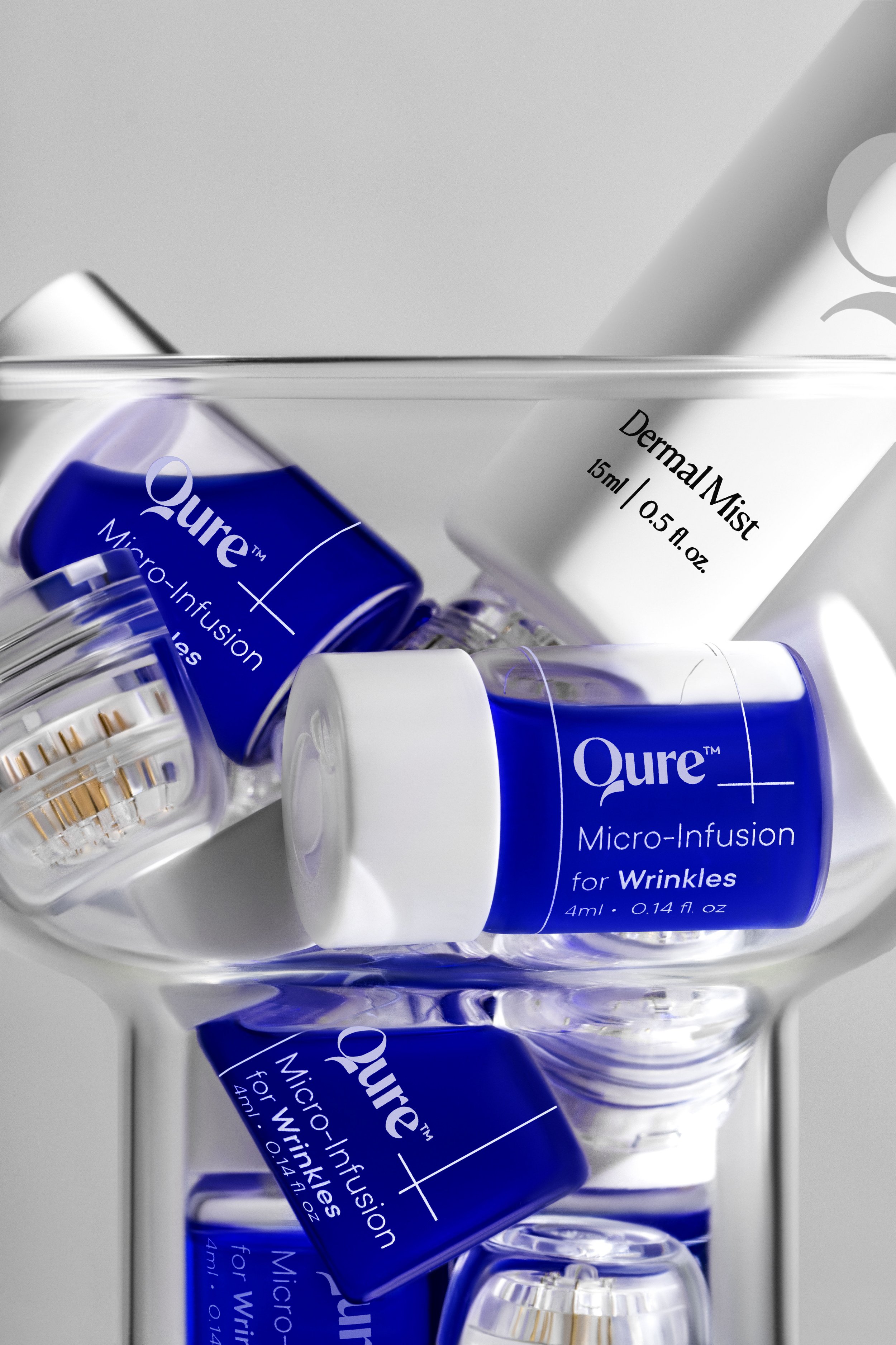 Close-up of beauty product bottles including Qure Micro-Infusion for Wrinkles and Qure Micro-Infusion for Winkles in a glass container.