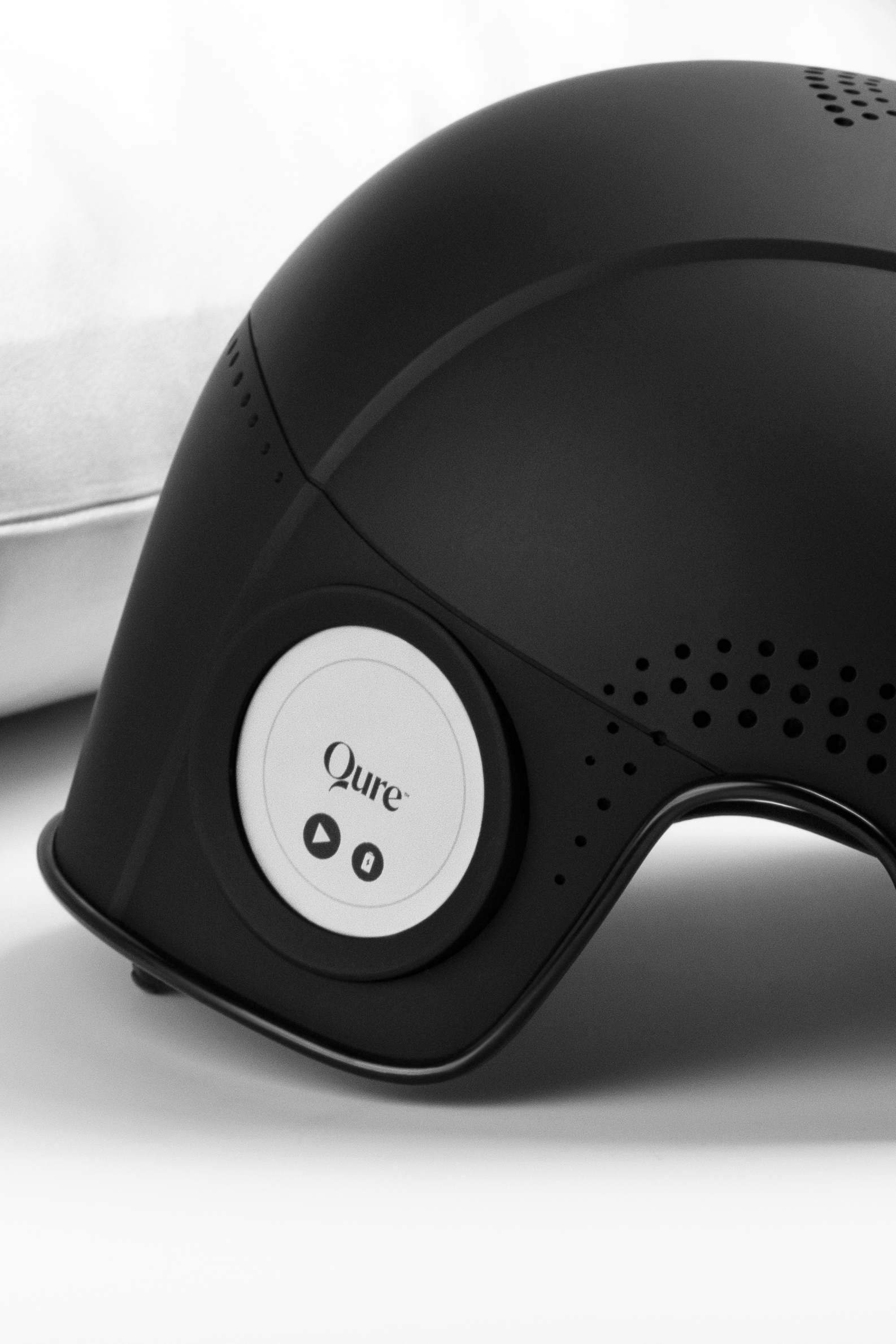 A black Qure device with a round display and control buttons on a white surface.