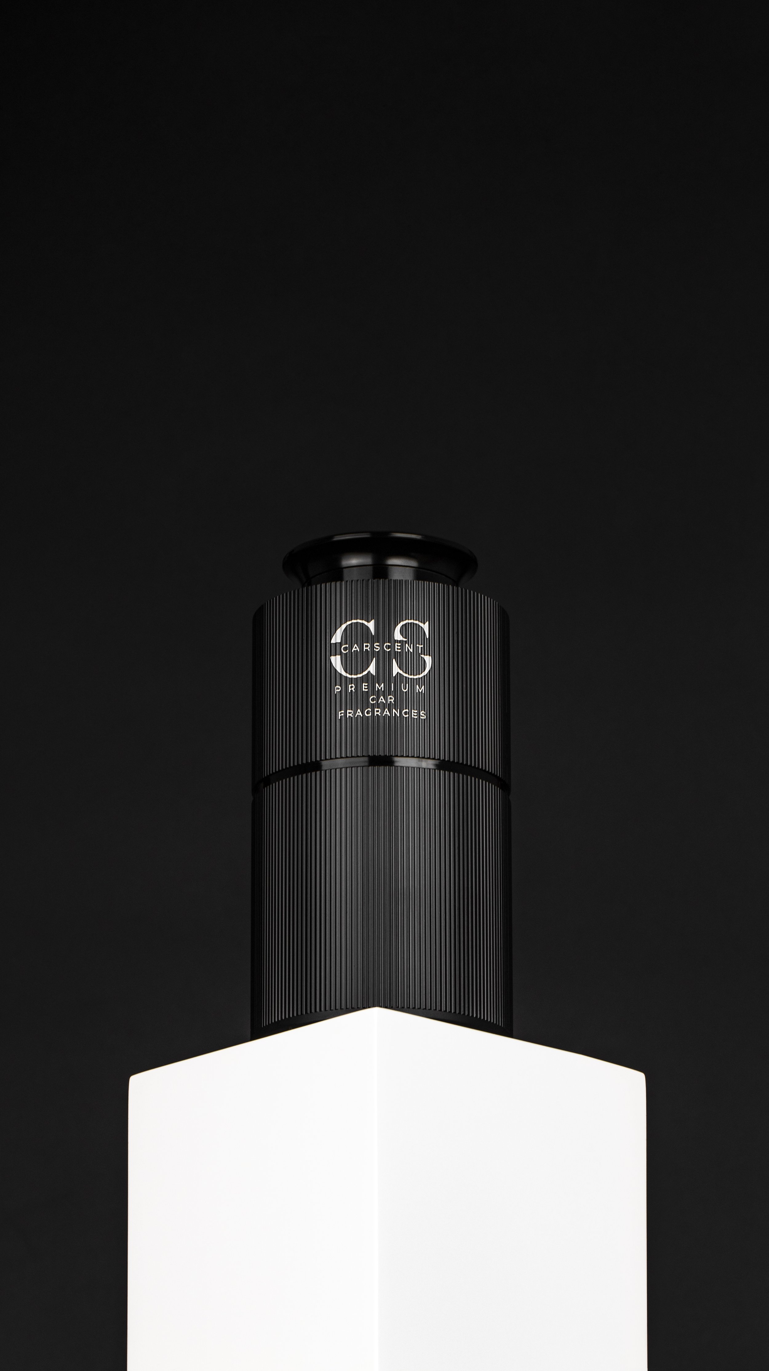 A black cylindrical container of car fragrance with the label 'Carscent Premium Car Fragrances' is placed on a white rectangular stand against a black background.