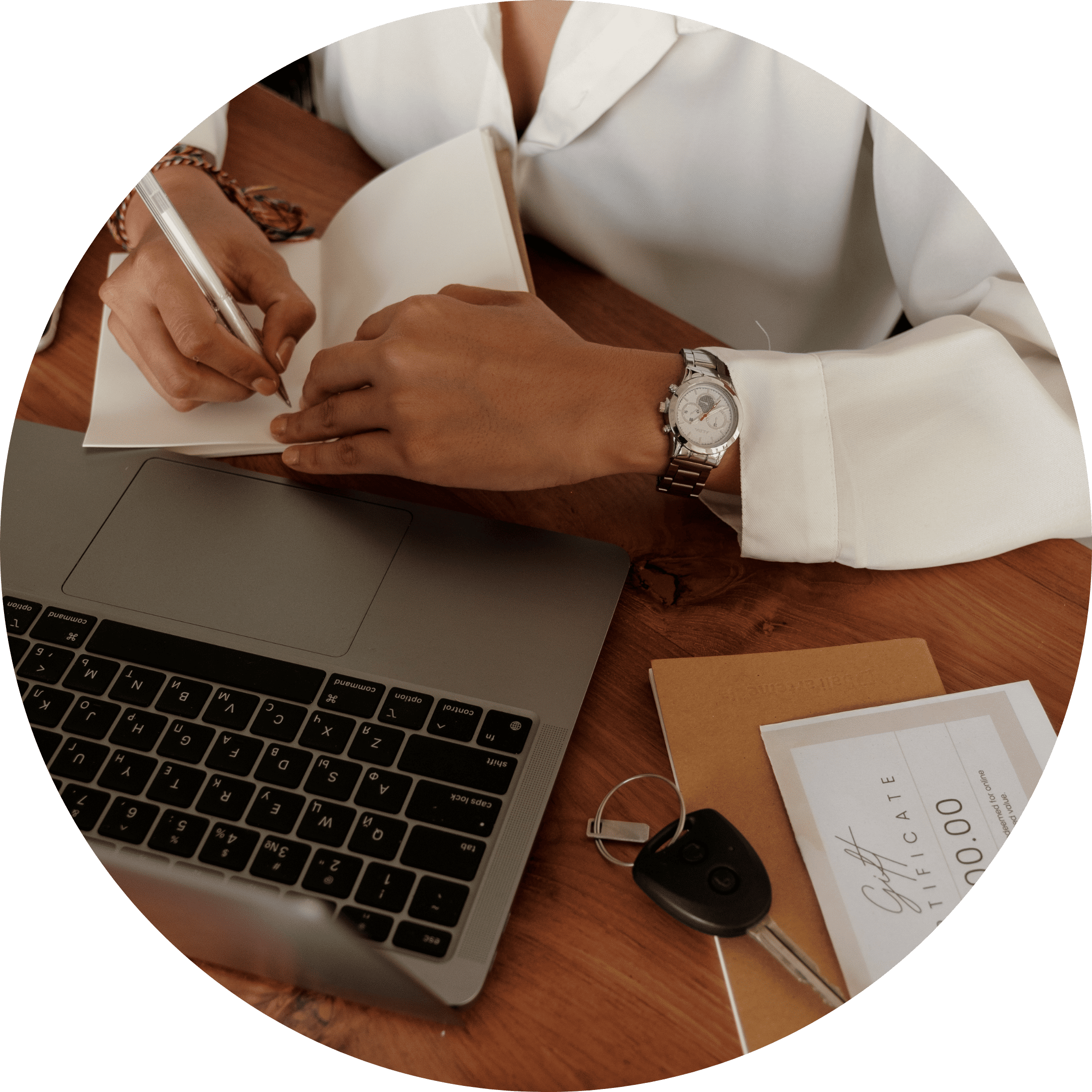 Person writing notes in a planner beside a laptop and documents.