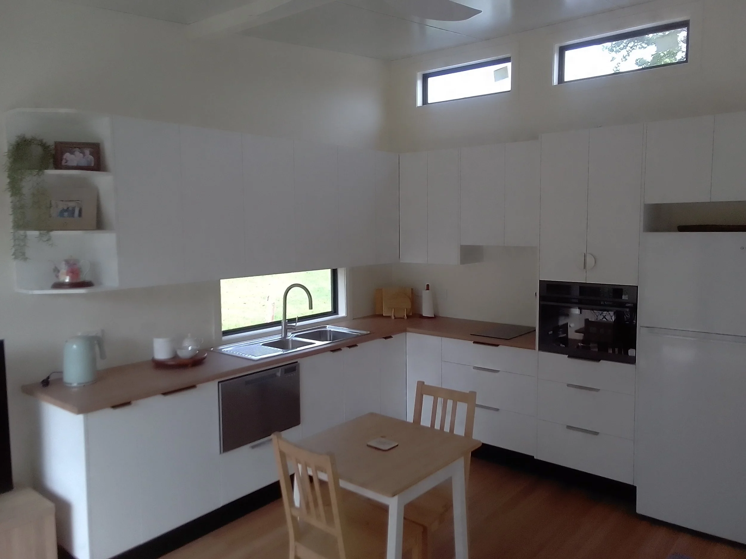 Modern kitchen with white cabinets, wooden countertops, a double sink, and two long horizontal windows.mid north coast modular homes scconstruction.online