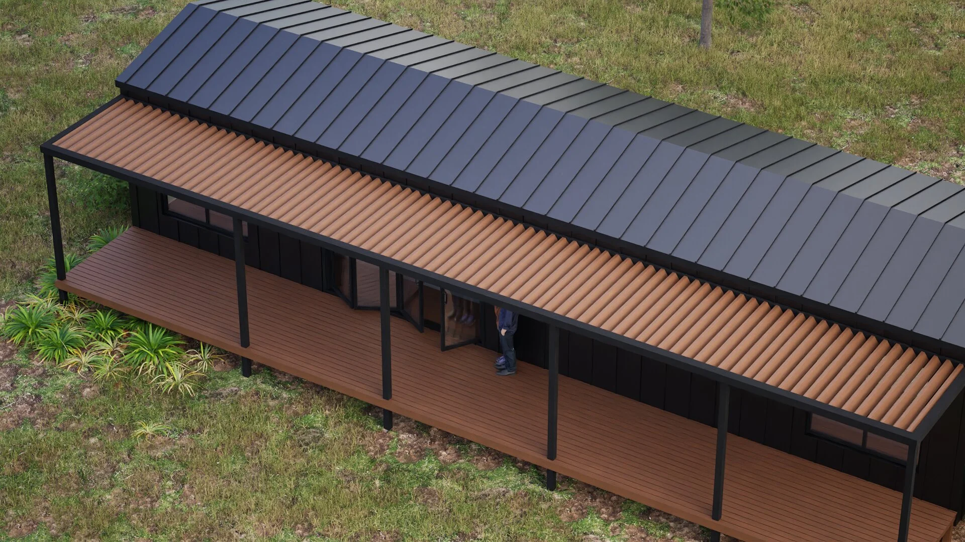 A modern house with a black roof, black walls, and brown wooden deck seen from above, with some plants and grass surrounding it.