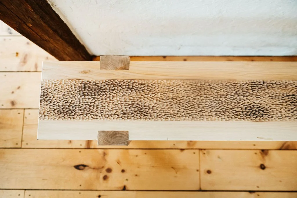 Close-up of a wooden surface with a central strip of small, rounded wooden pegs or beads, and a light-colored wood border around it.
