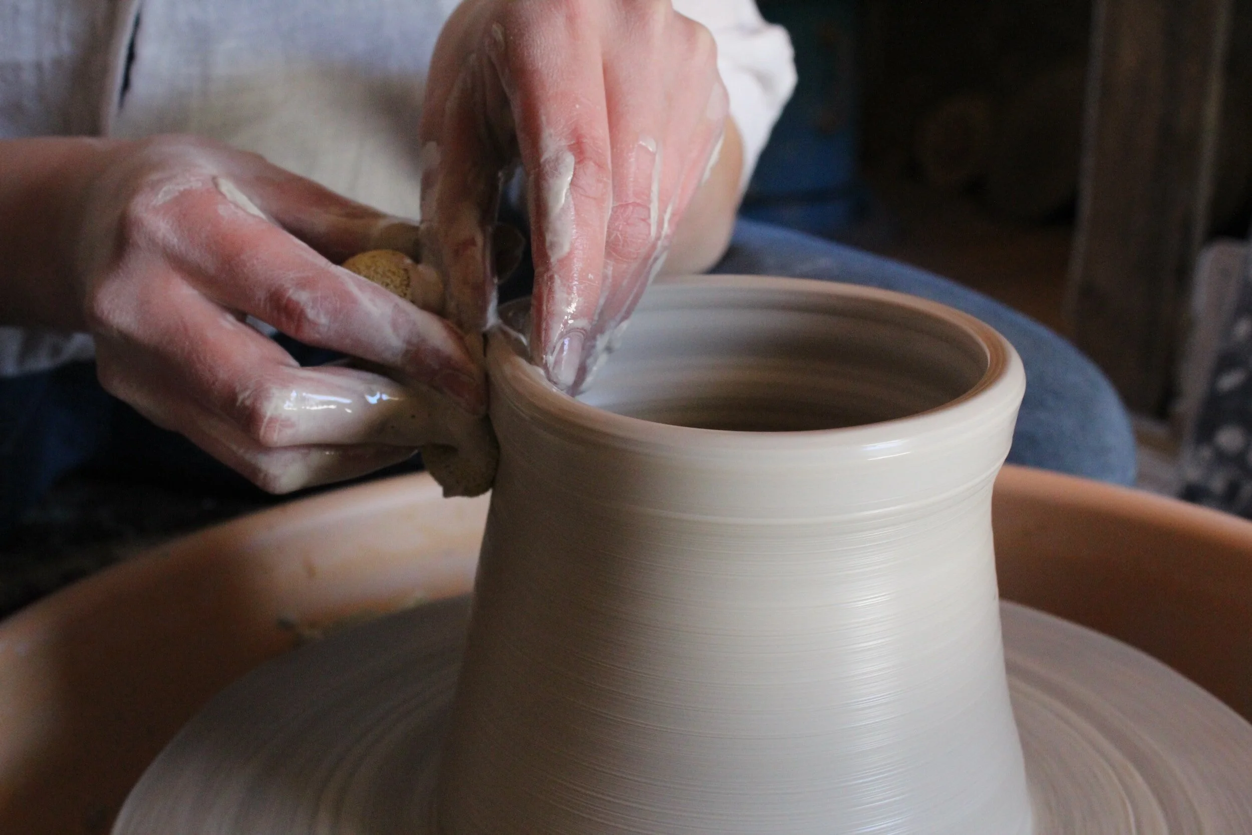 Hands shaping clay on a pottery wheel