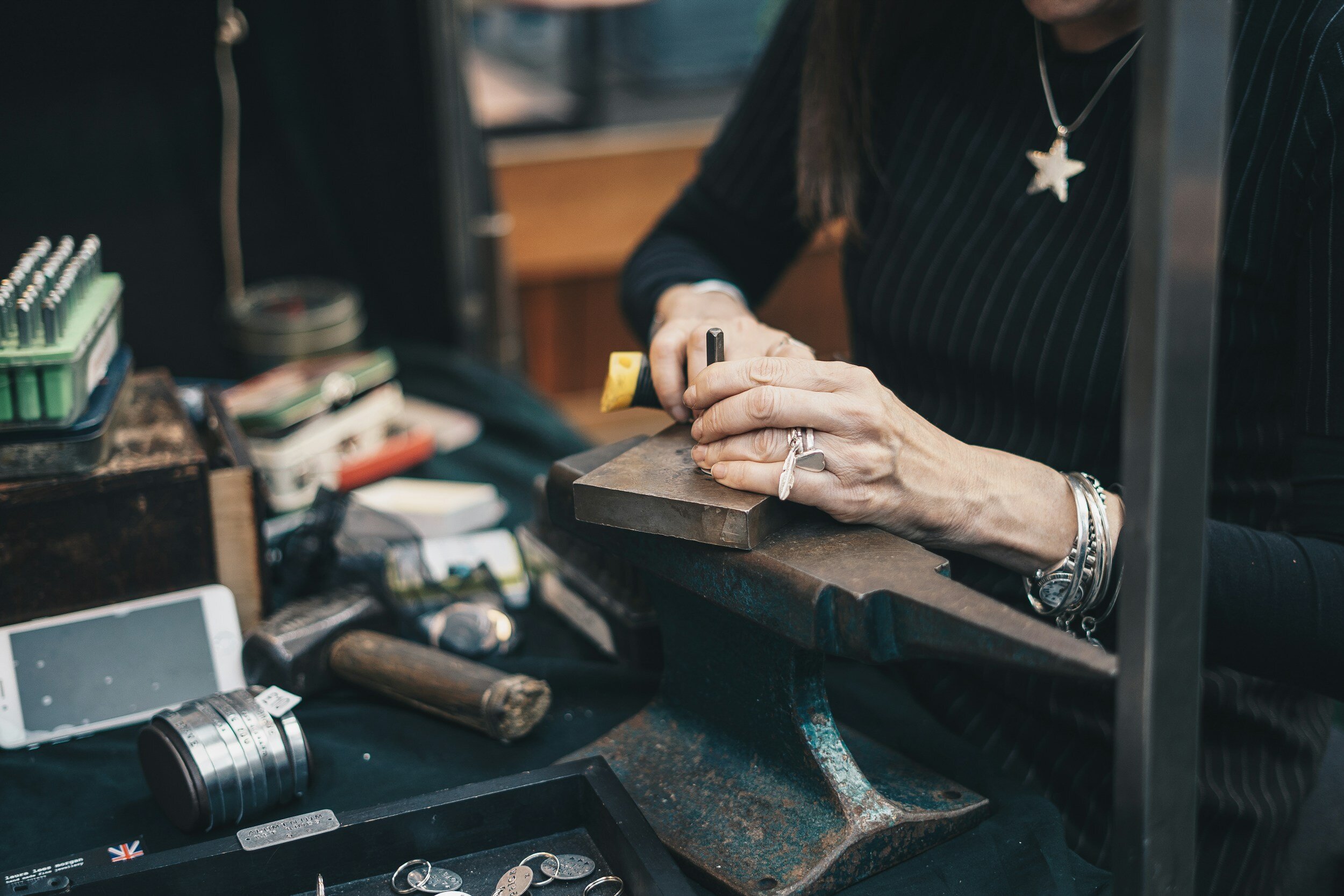 Person crafting jewelry on an anvil with tools and materials on a table