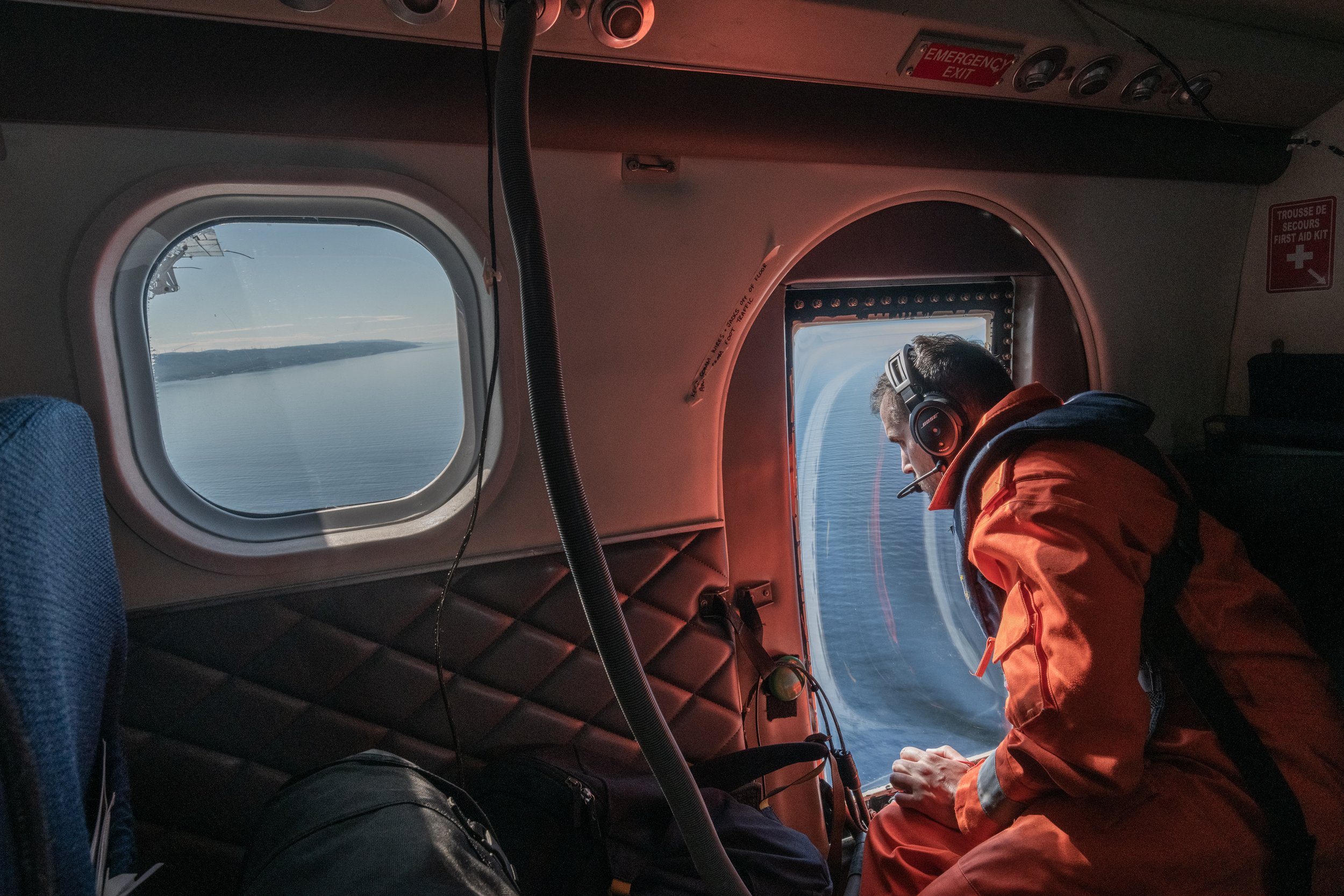 Samuel Mongrain, a survey technician with Fisheries and Oceans Canada, gazes out the specially modified window of a Twin Otter airplane. His team gathers vital data on right whale locations to inform management decisions on shipping and fishing activ