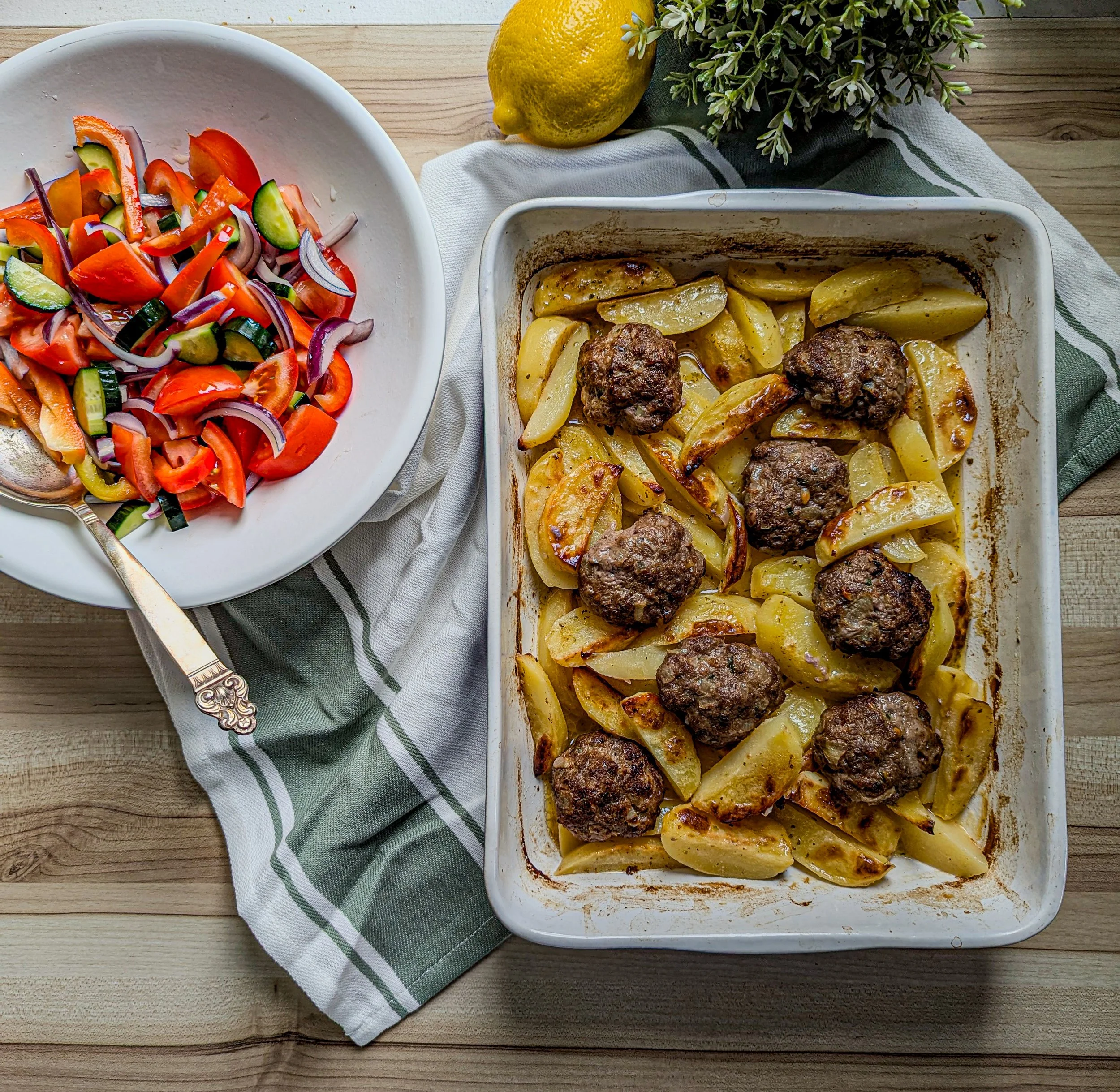 Baked dish with greek meatballs and roasted potatoes, served with a Greek salad on the side with tomatoes, cucumbers, green peppers & red onions.