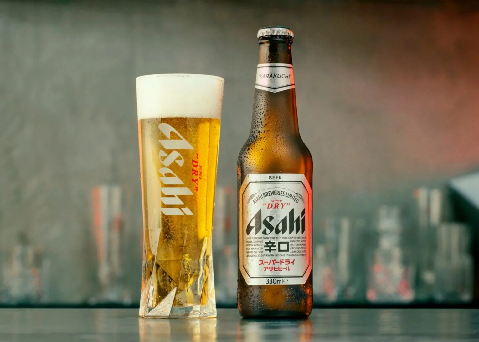 A bottle of Asahi beer and a glass filled with beer on a table against a blurred background.