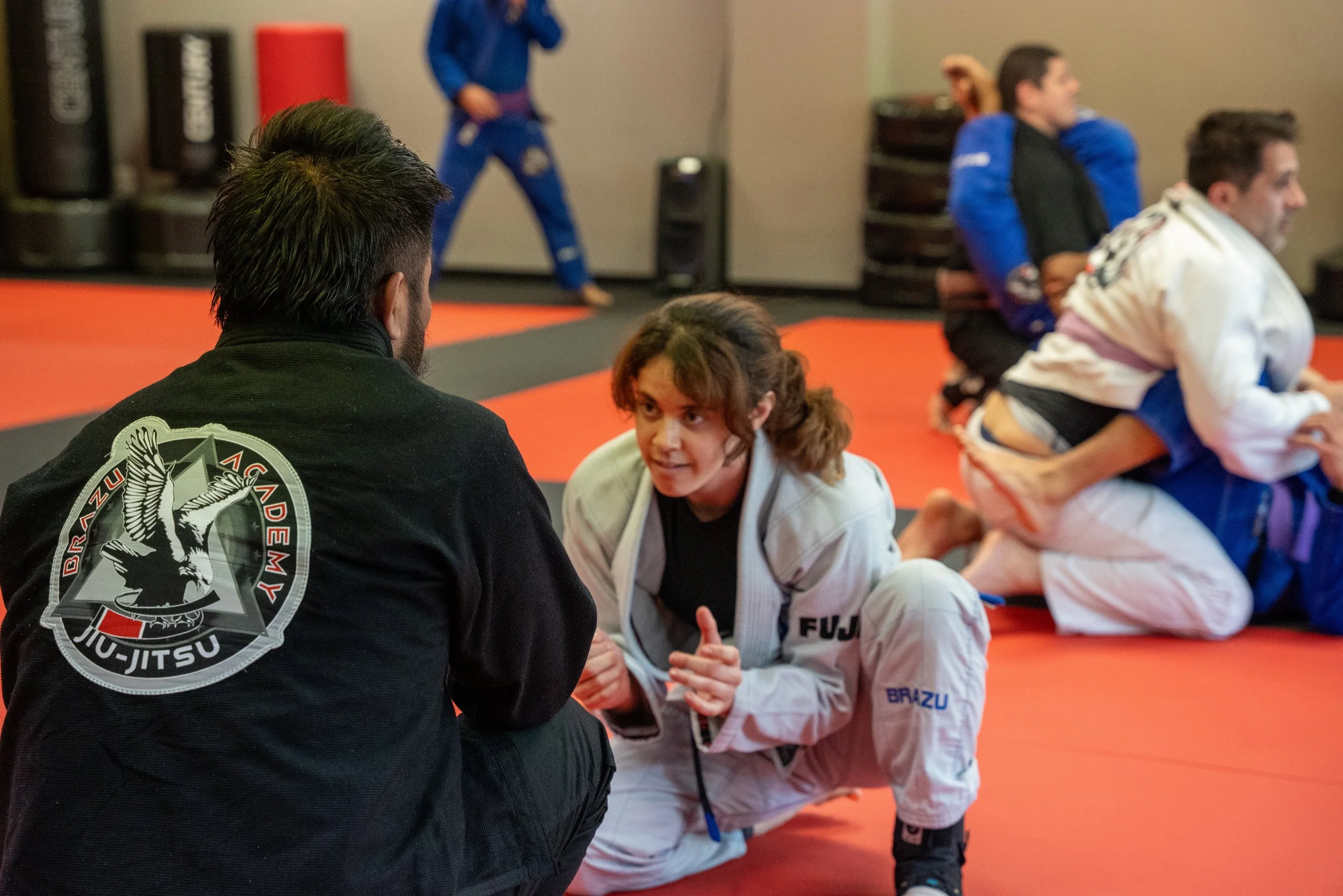 Brazilian Jiu-Jitsu class with students practicing techniques on the mat, listening to the instructor.