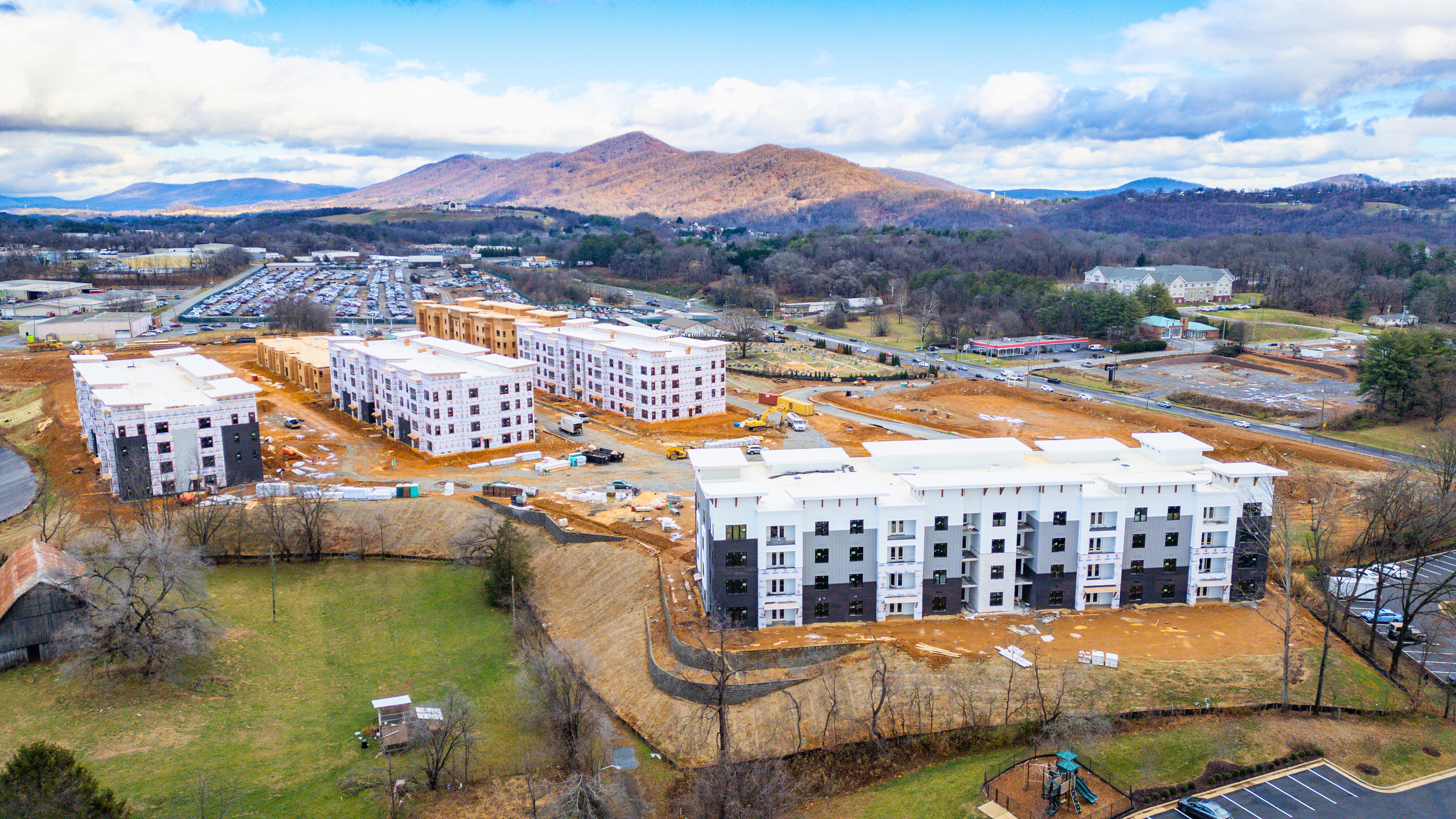 Aerial view of a modern white apartment complex with multiple buildings, parking lots, and surrounding greenery.
