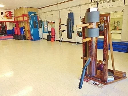 Martial arts school showing wooden dummy in foreground and punching bags hanging from rail in background.