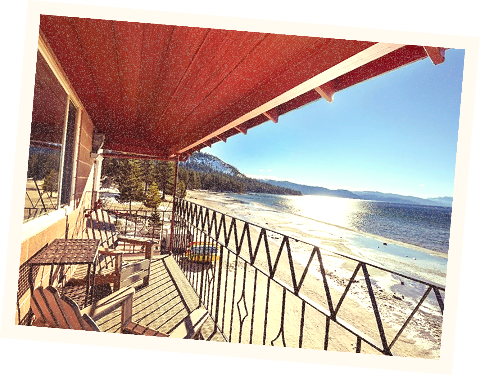 Beach view from a balcony with chairs and a railing, overlooking the ocean, mountains, and clear blue sky.