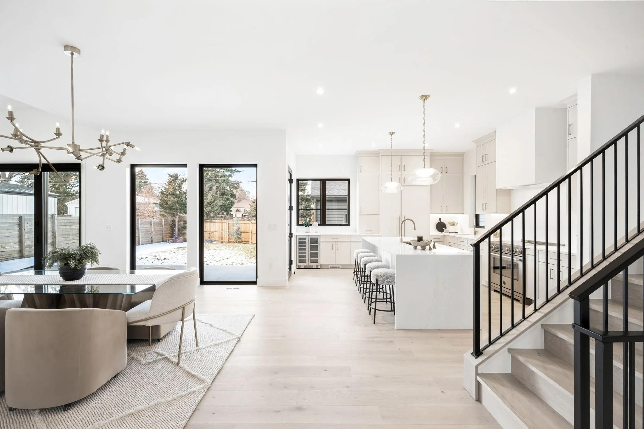 Bright, open-concept kitchen and dining area with white cabinets, island, and modern lighting, overlooking a backyard through large sliding glass doors.
