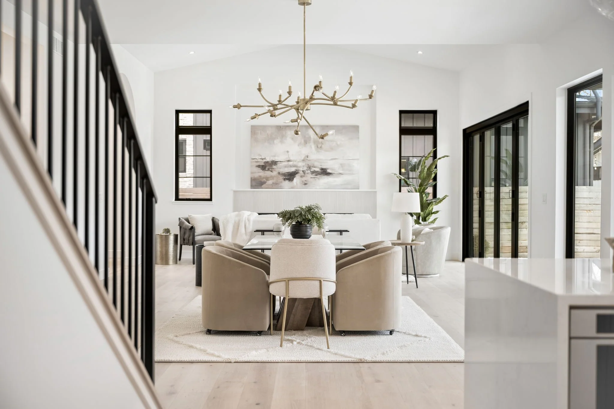 Bright open-concept living room with white walls, beige furniture, black window frames, and a modern chandelier.