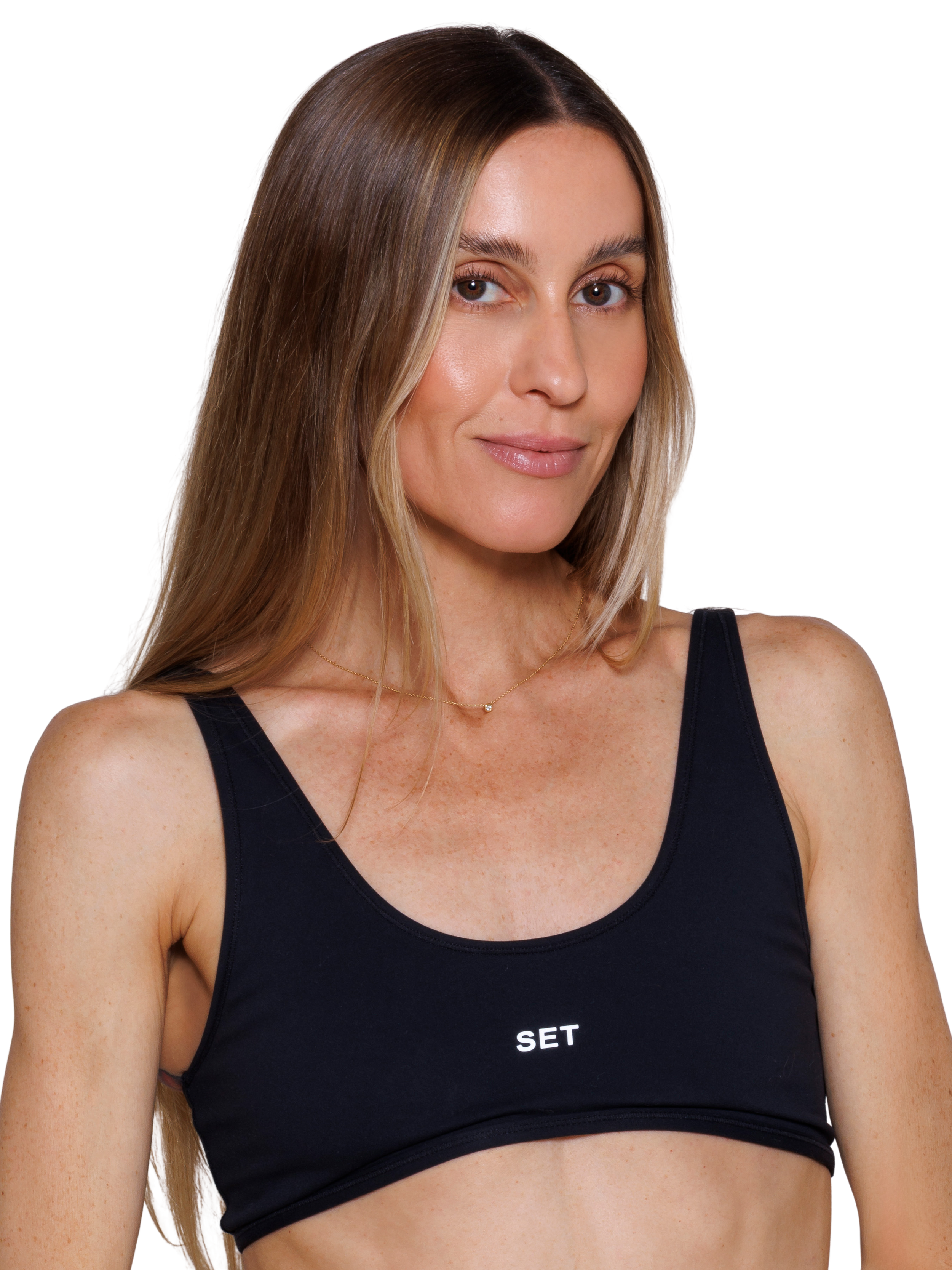 A woman with long blonde hair wearing a black sports bra that says "SET", softly smiling at the camera