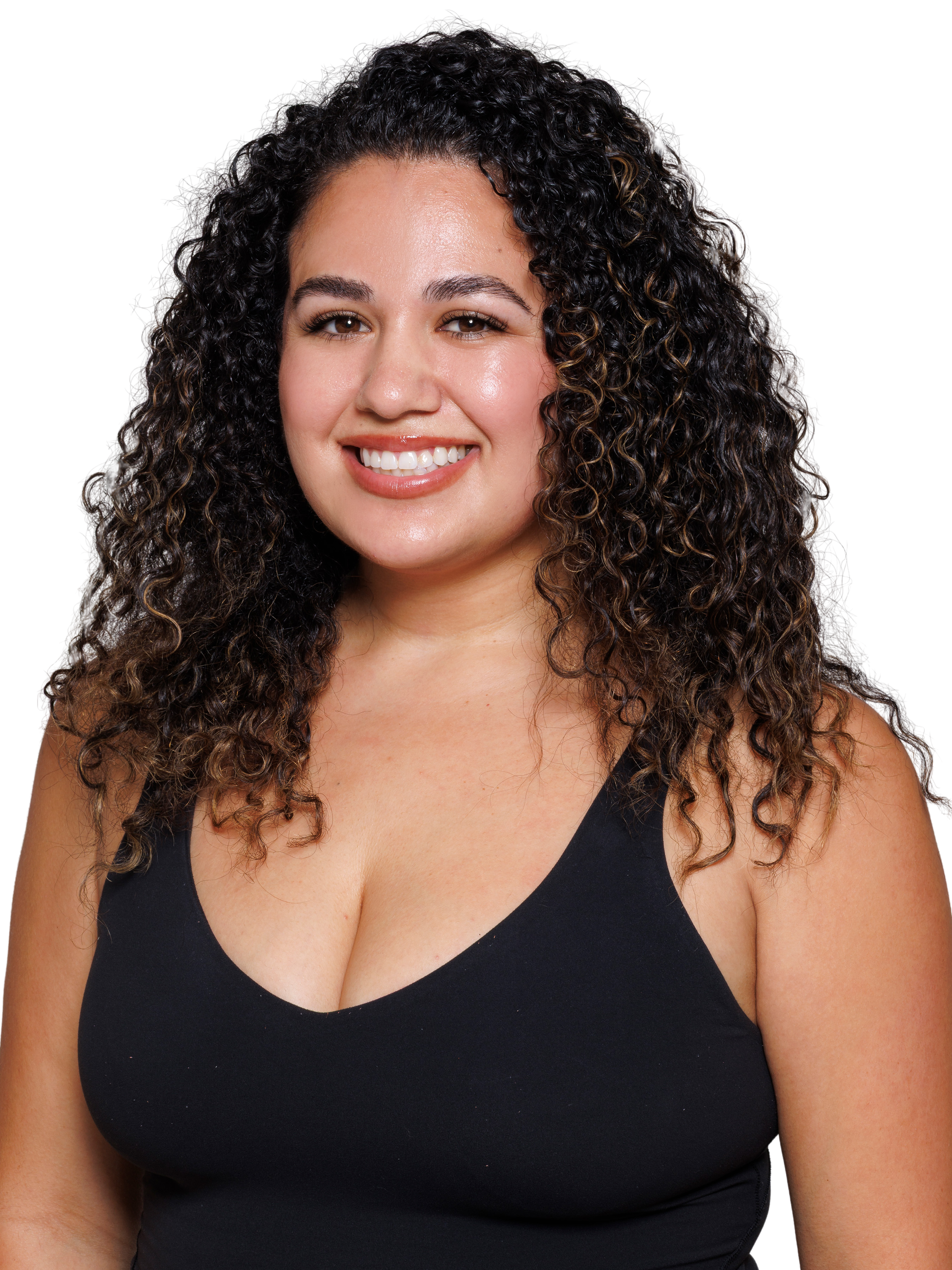 A young woman with curly hair in a ponytail, wearing a black sleeveless top, smiling and standing with her hand on her hip, accessorized with gold hoop earrings, a necklace, and a smartwatch.