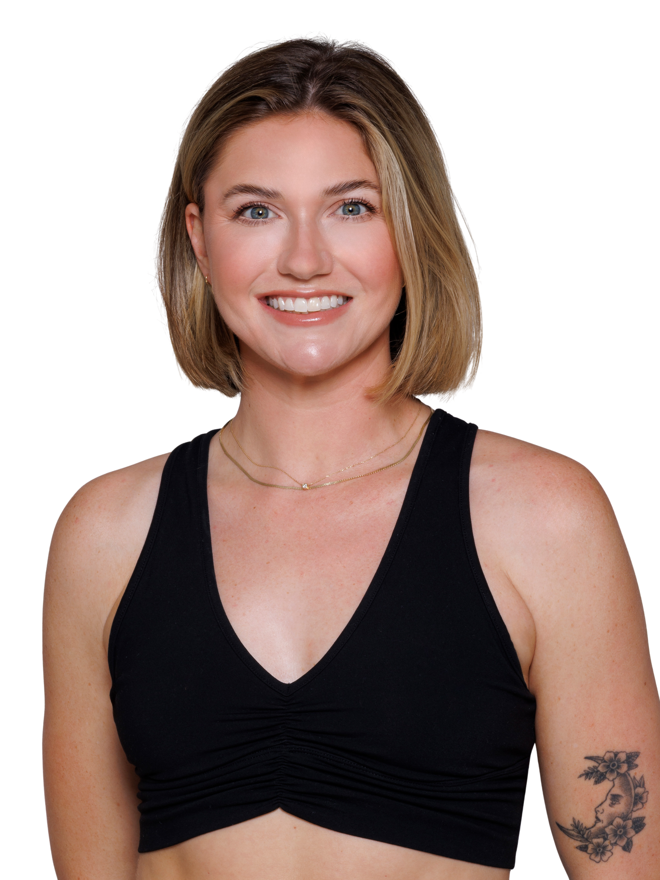 A young woman with short, wavy brown hair smiling, wearing a black sports bra, standing with her hand on her hip, against a white background.