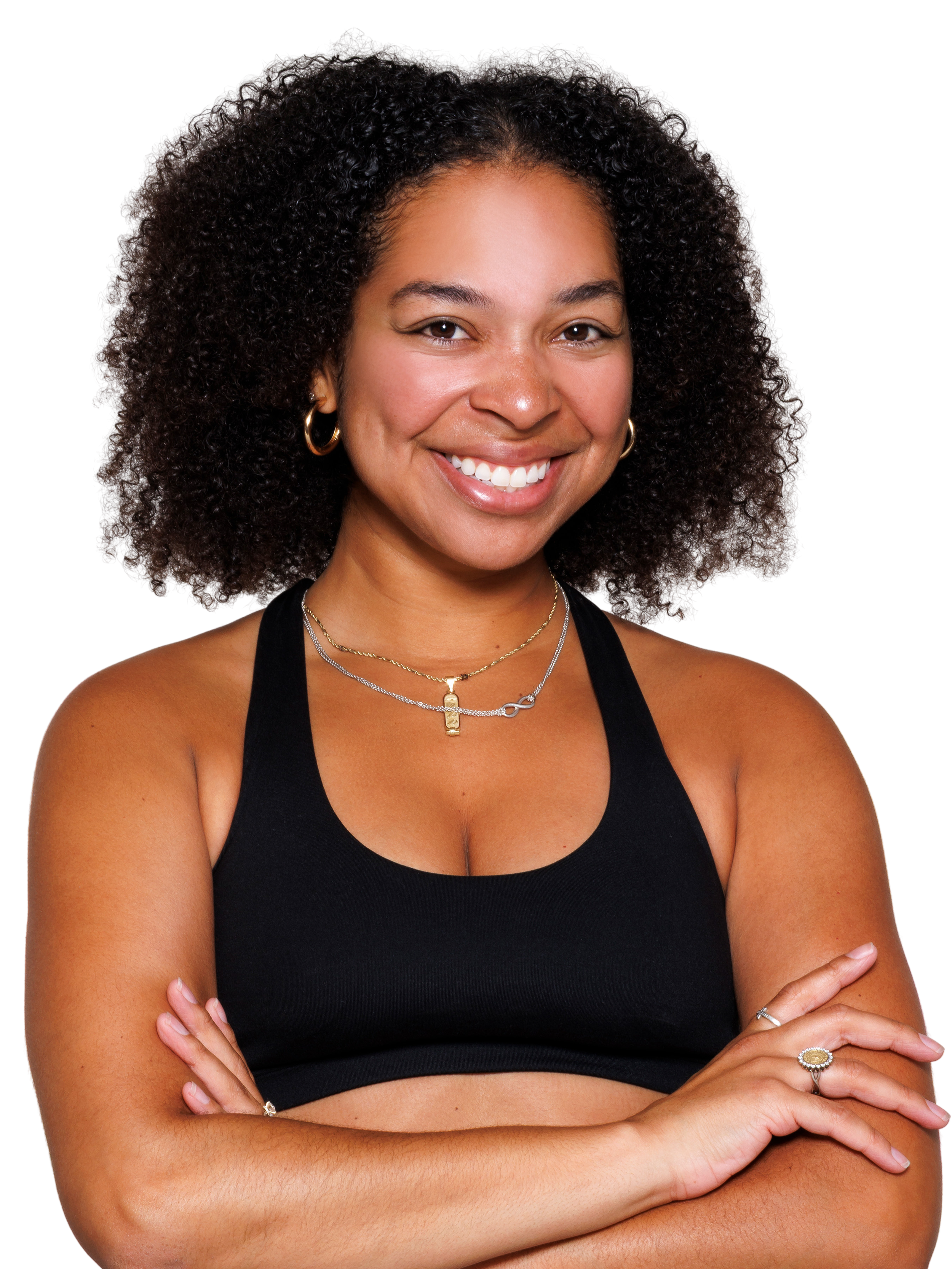 A woman with shoulder-length curly hair wearing a black crop workout top, crossing her arms and smiling at the camera