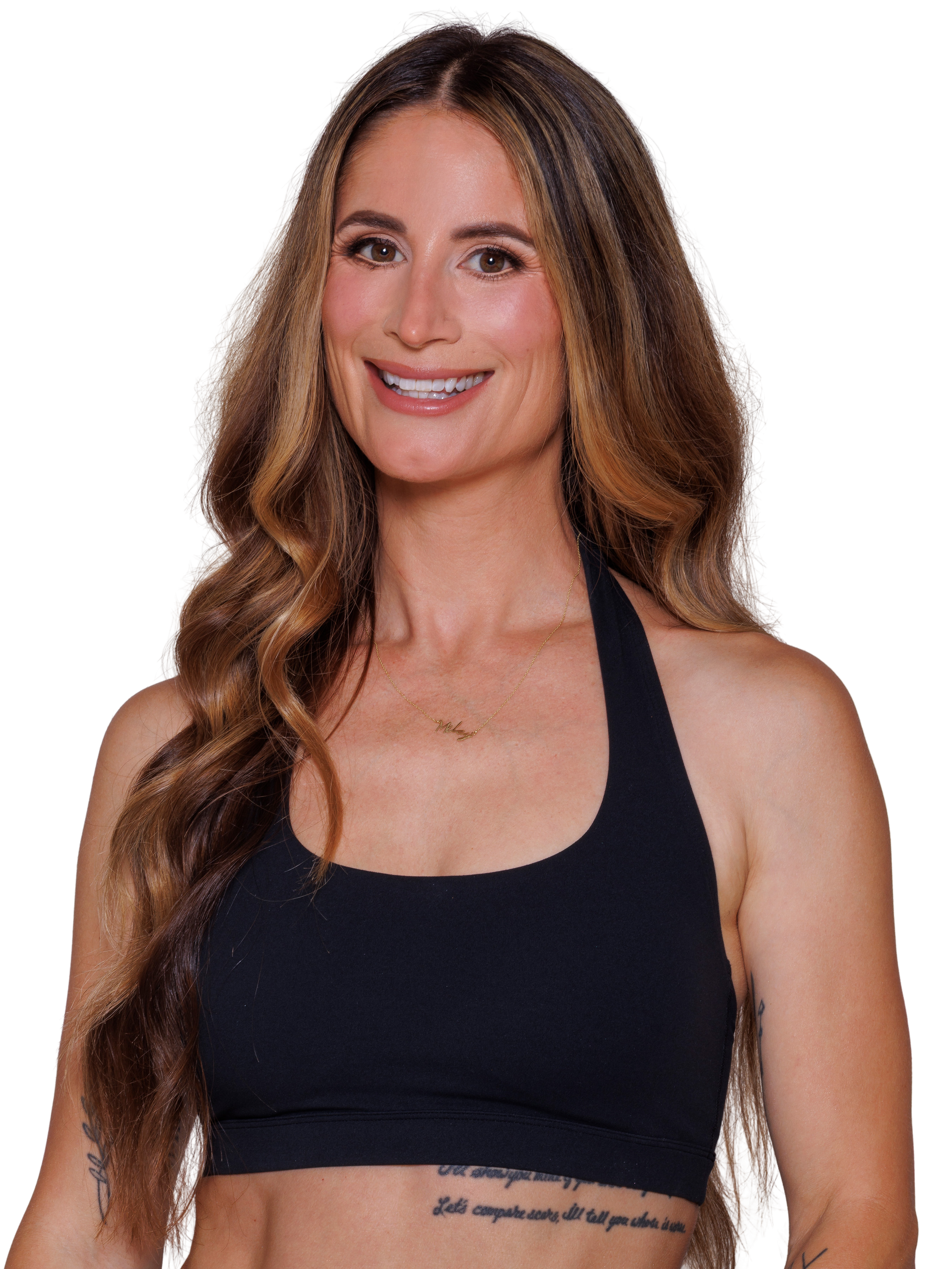 A woman with long curly brown hair, wearing a black sleeveless workout crop top and smiles at the camera.