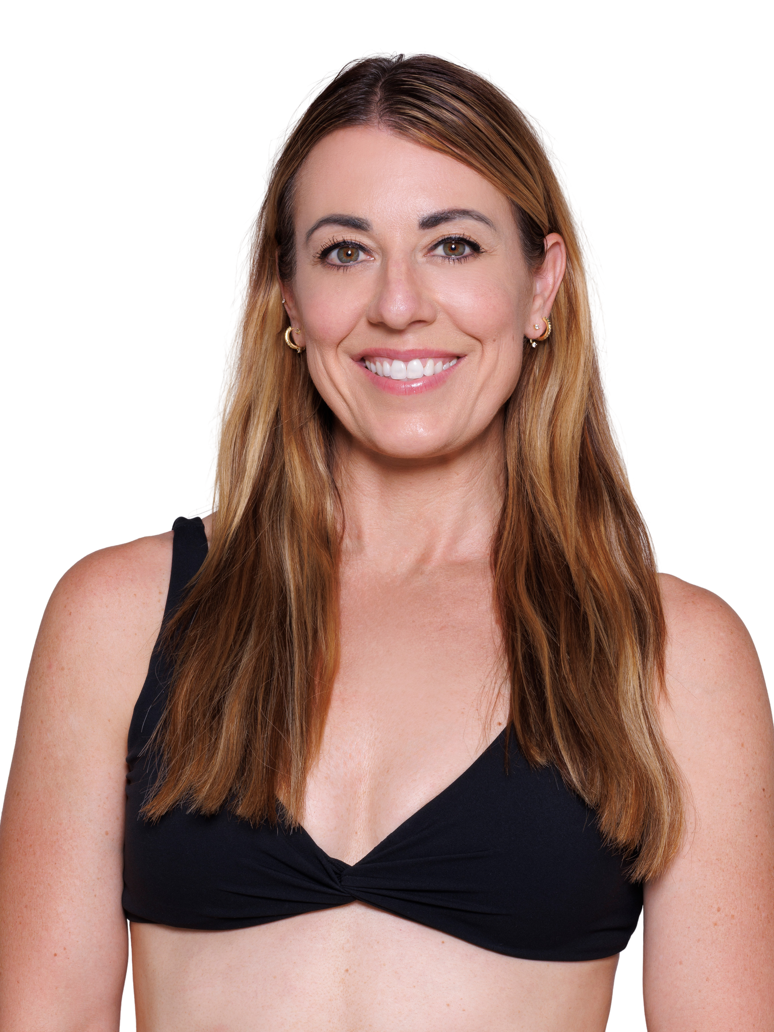 Happy woman with long, light brown hair wearing a black sports bra and black workout pants, smiling with her hand on her hip.