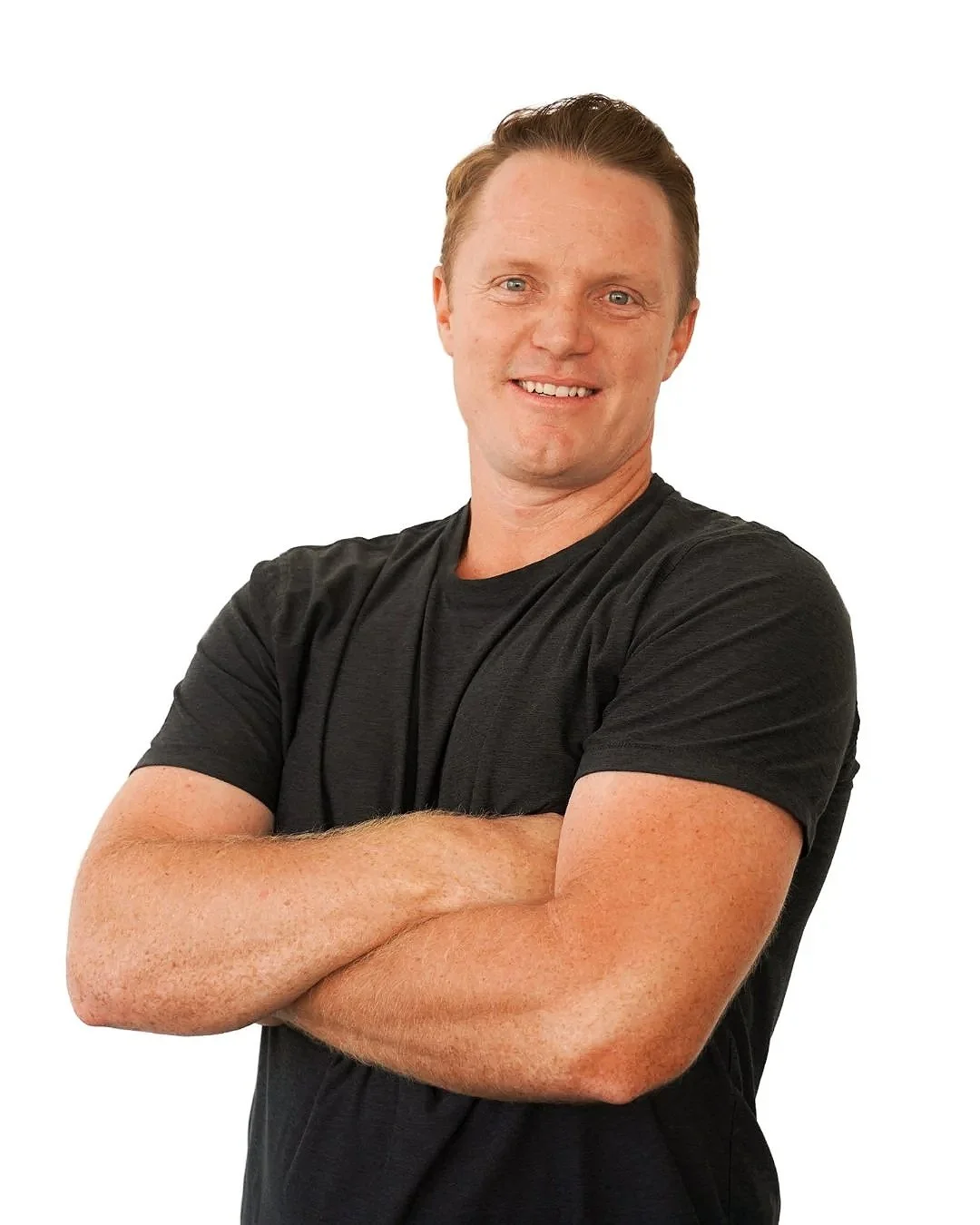 A smiling man with short, light brown hair, wearing a black T-shirt, standing with arms crossed against a plain white background.
