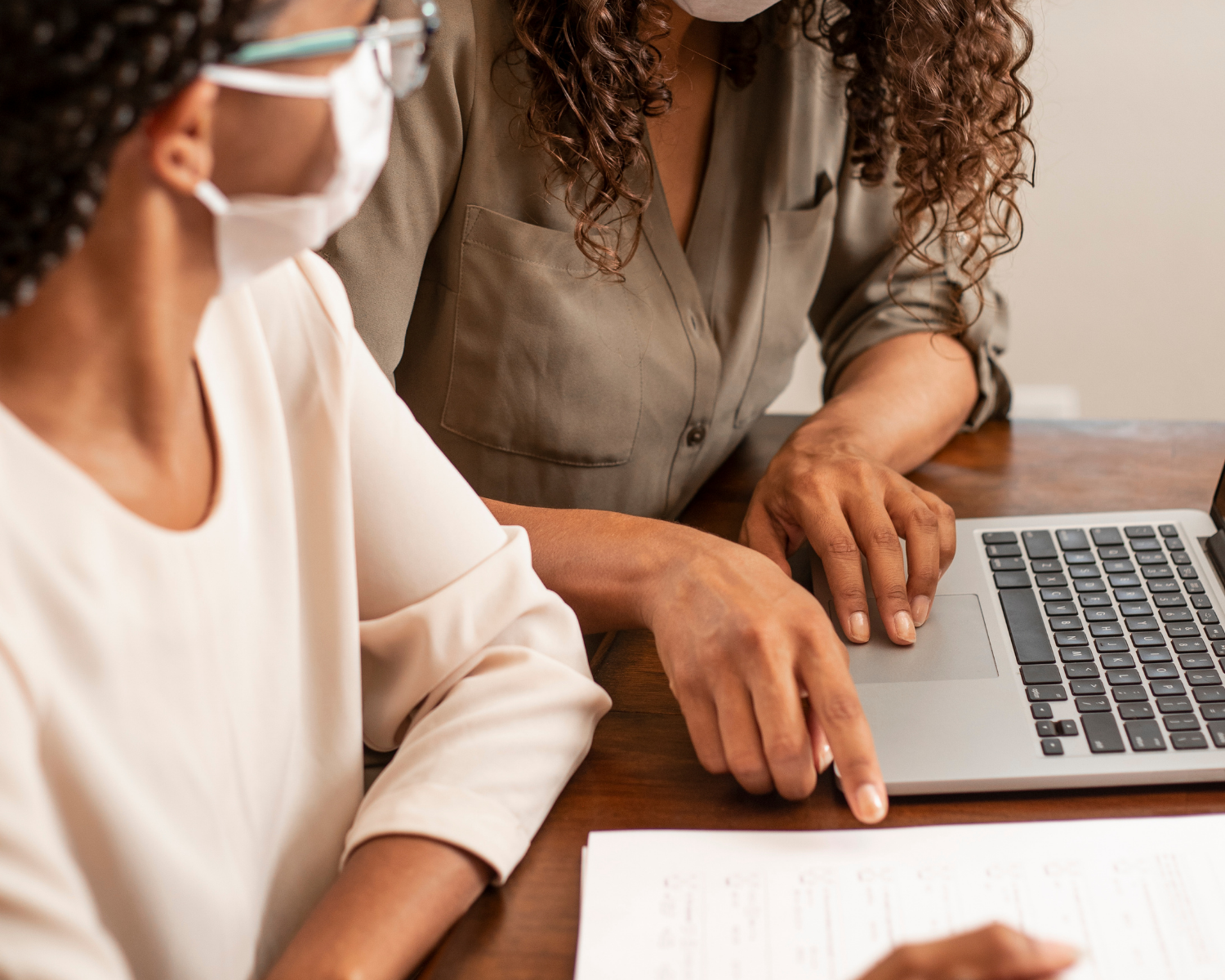 Two people sit at a table going over a document. One is poised with a pen while the other points out key information for them to consider.