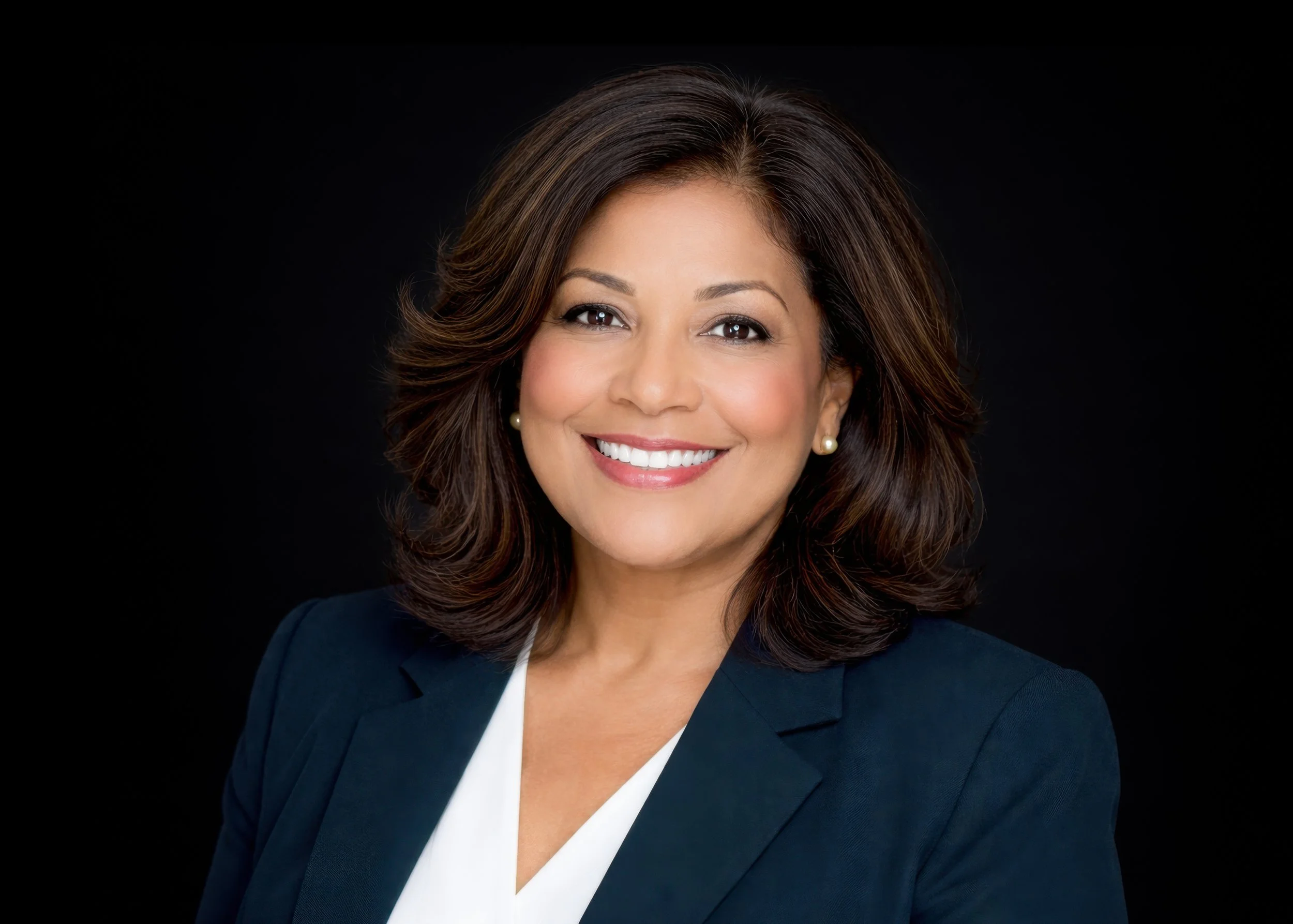Professional headshot of a woman with shoulder-length dark brown hair, wearing a dark blazer and white top, smiling.