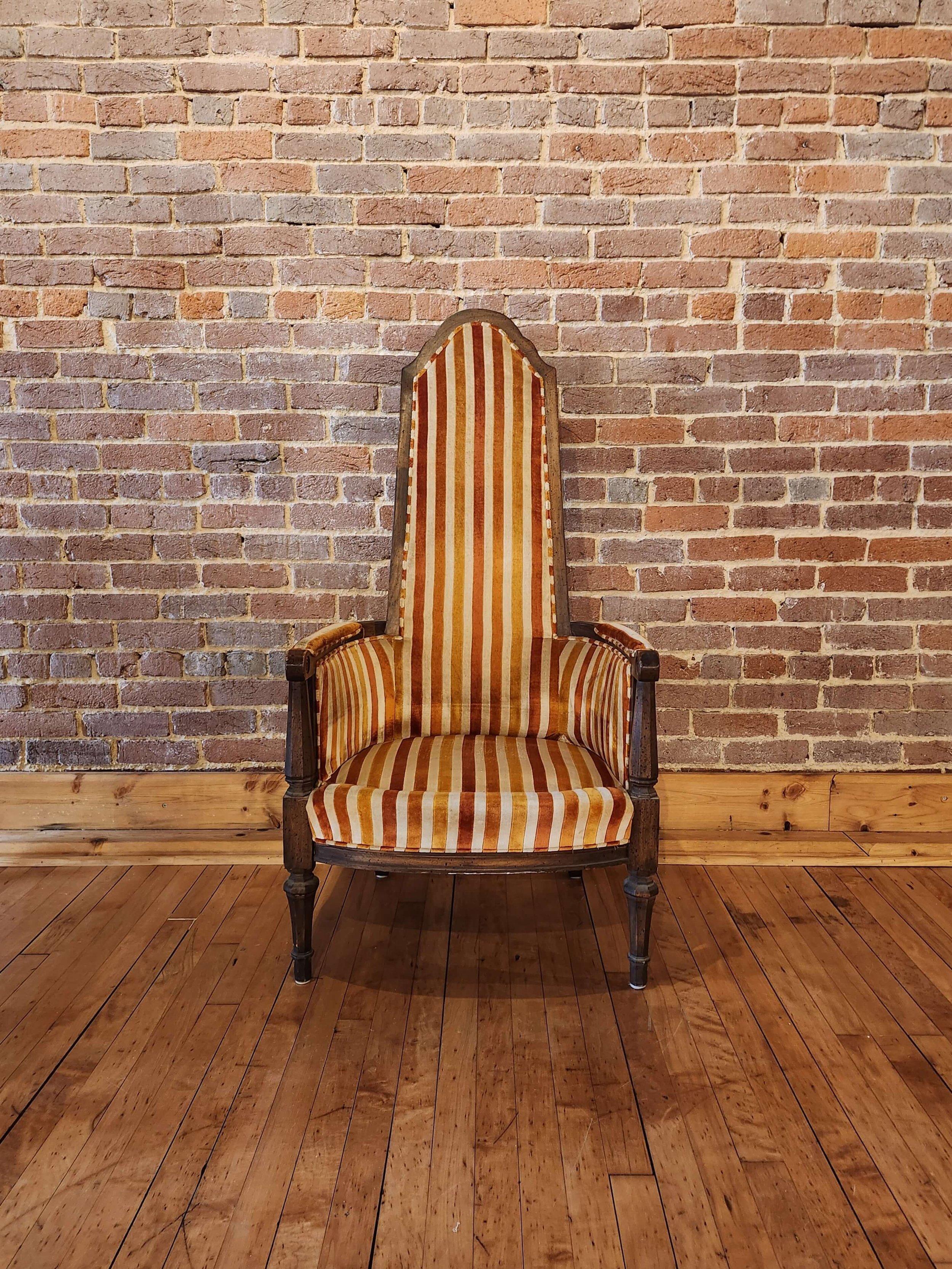 An antique high-back armchair with striped orange and cream fabric, placed against a brick wall on a wooden floor.