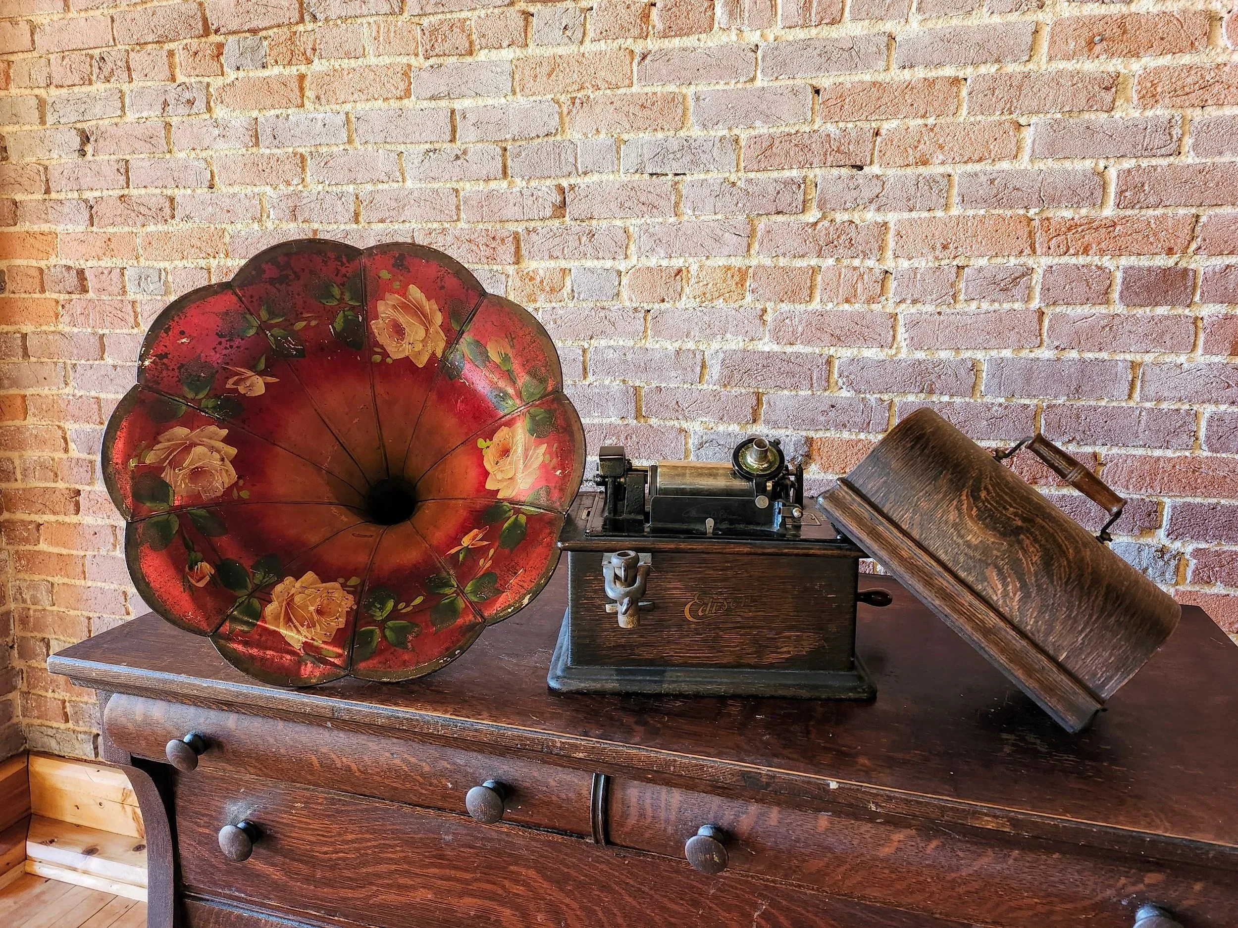 Vintage gramophone with a large red floral horn on a wooden table against a brick wall.