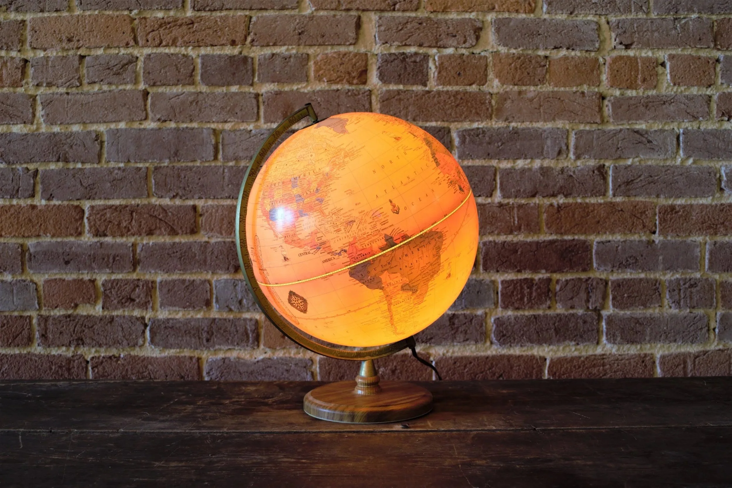 Illuminated globe emitting a warm glow, placed on a wooden surface against a brick wall background.