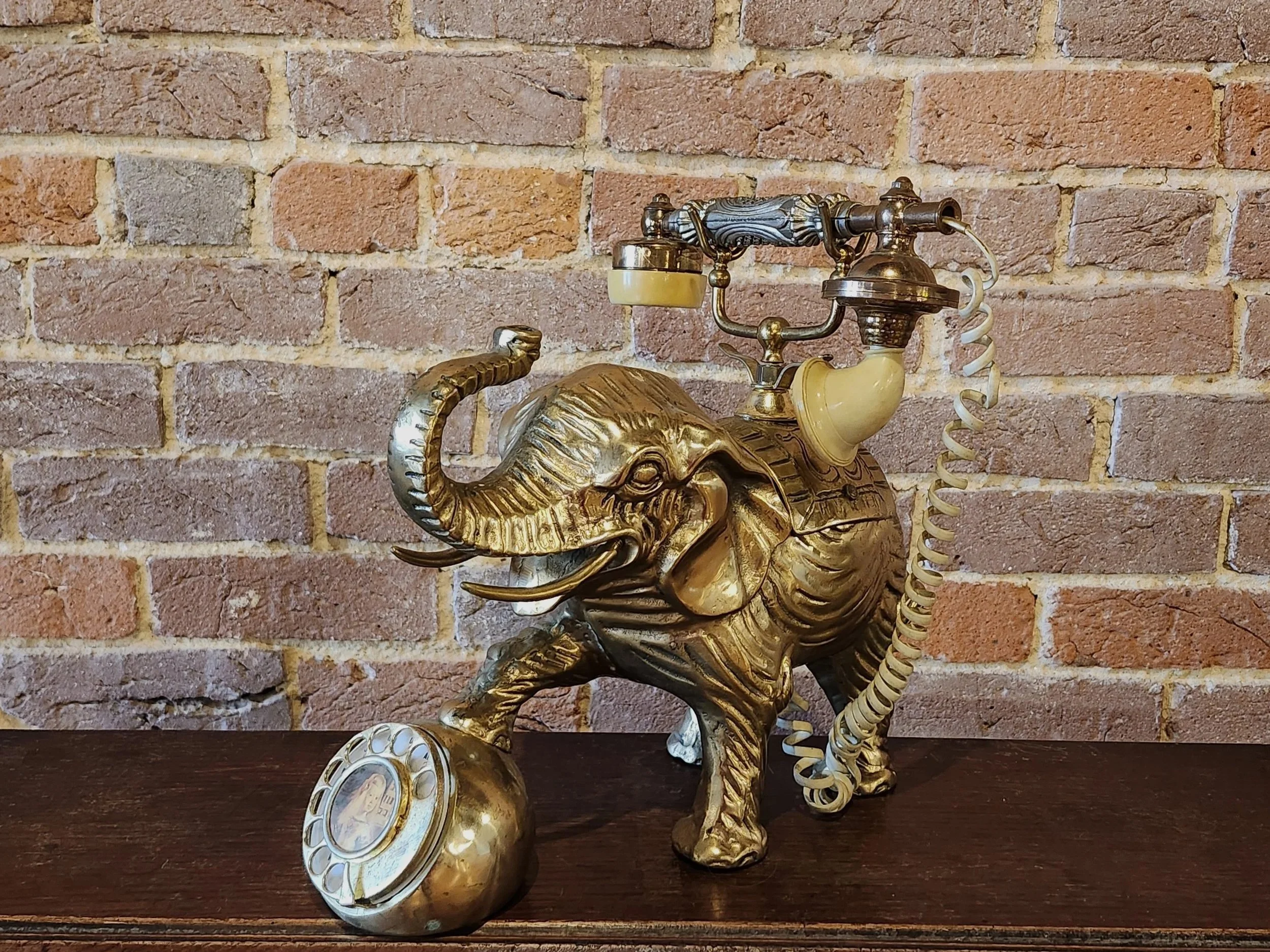A vintage-style desk telephone designed as a golden elephant against a brick wall background.
