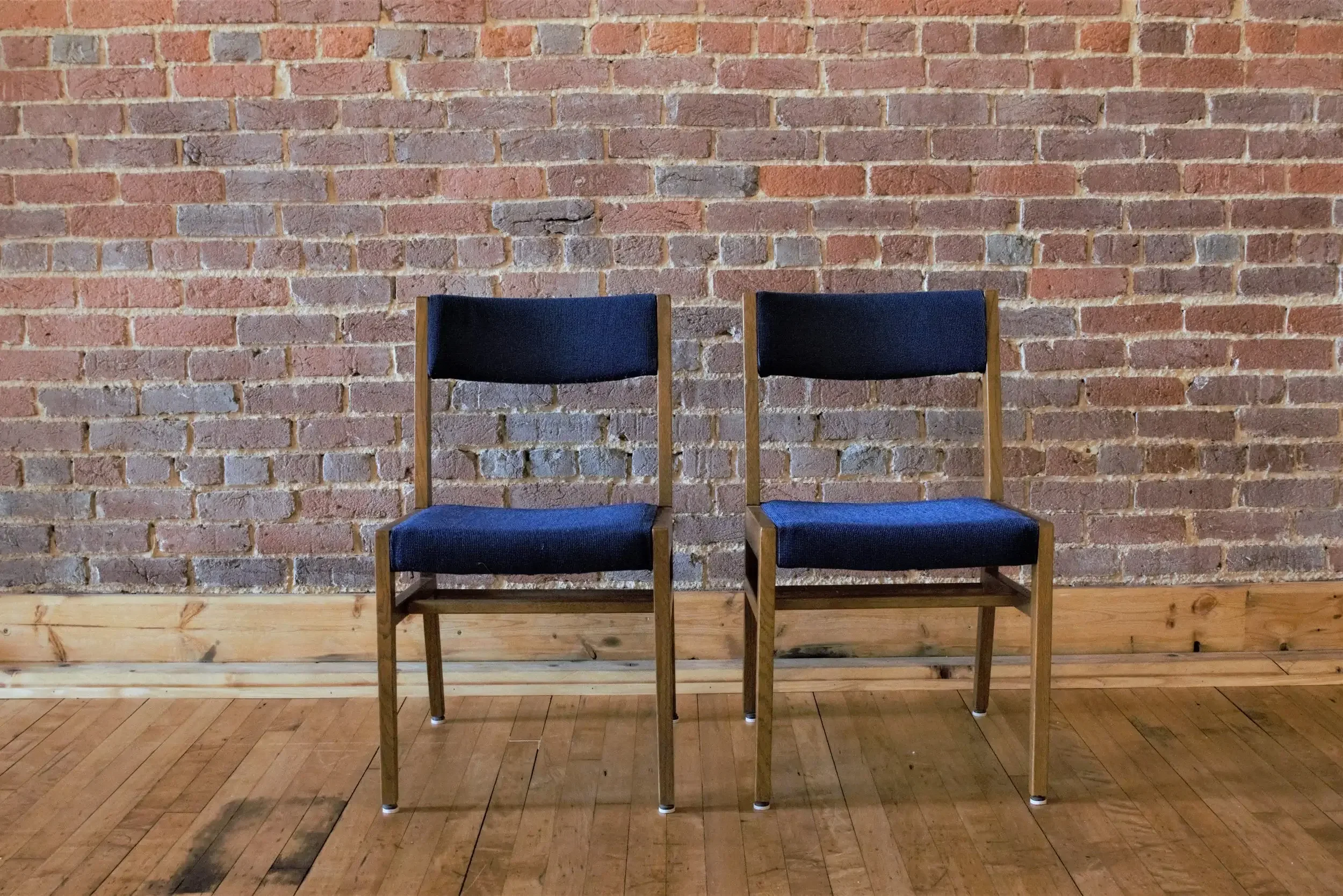 Two black and wooden chairs placed against a brick wall on a wooden floor.