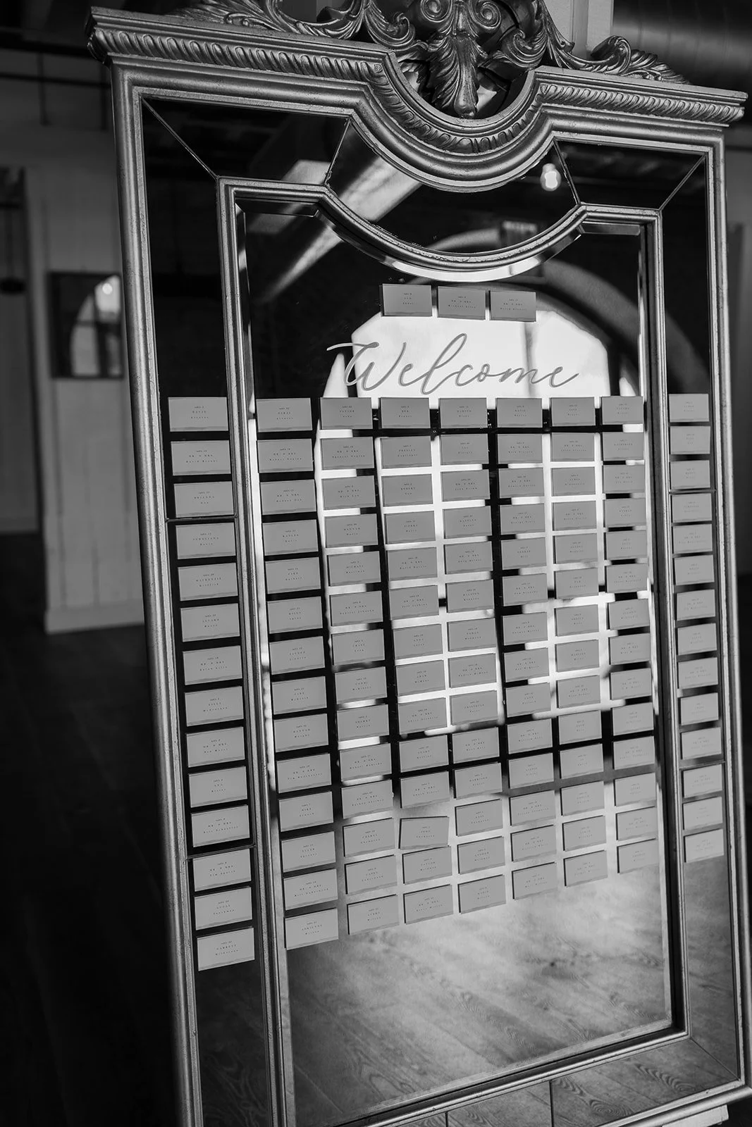 An ornate, vintage mirror frame used as a photo backdrop with numerous small cards pinned to it, and the word 'Welcome' written at the top center.