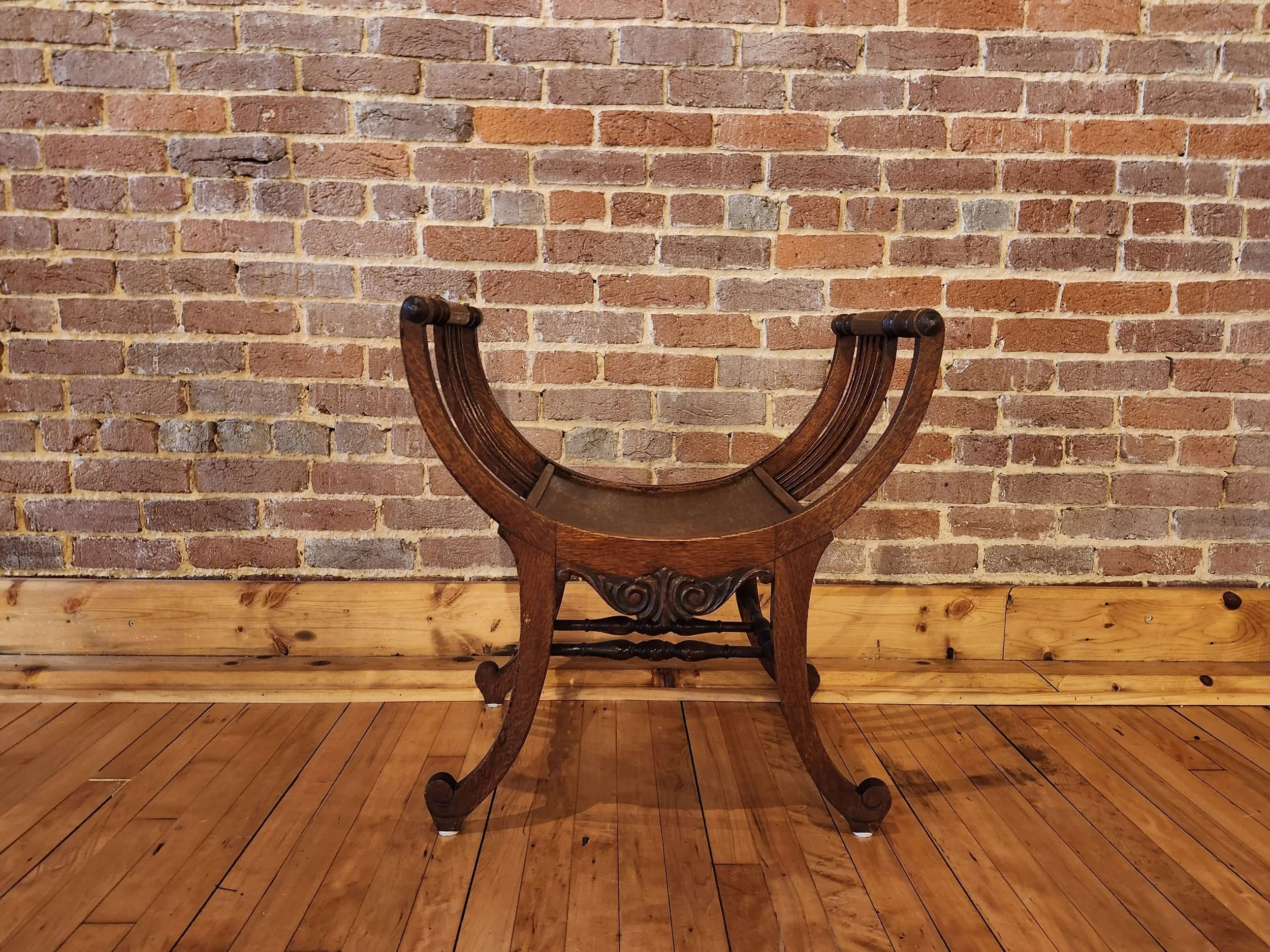 Upside-down wooden table with curved legs and a decorative carved apron, placed against a brick wall on a wooden floor.