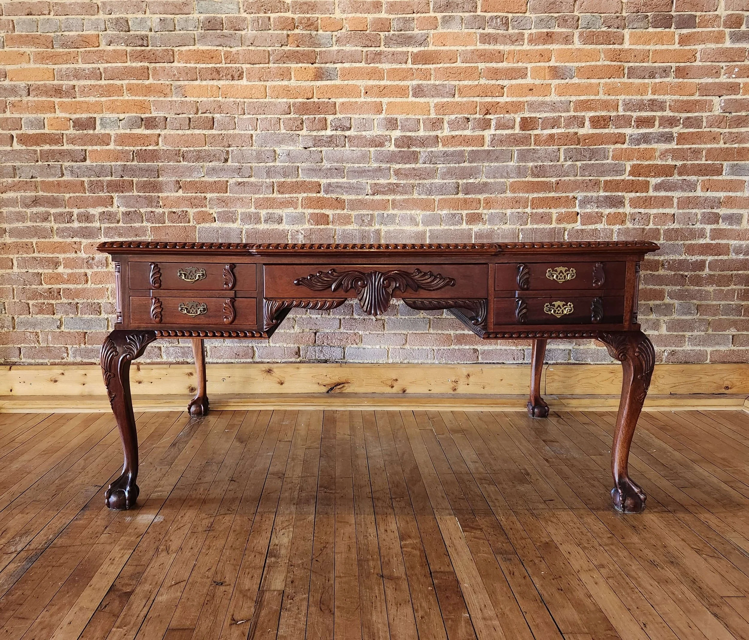 A vintage wooden desk with ornate carvings and brass handles, set against a brick wall and hardwood floor.